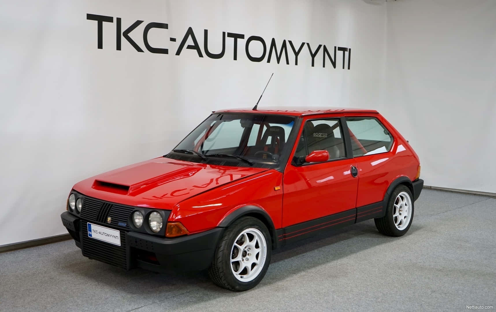 Fiat Ritmo 桌布 壁紙 — 一輛鮮紅色經典掀背車搭配白色車輪，在室內白色牆壁前展示，牆上有黑色文字。