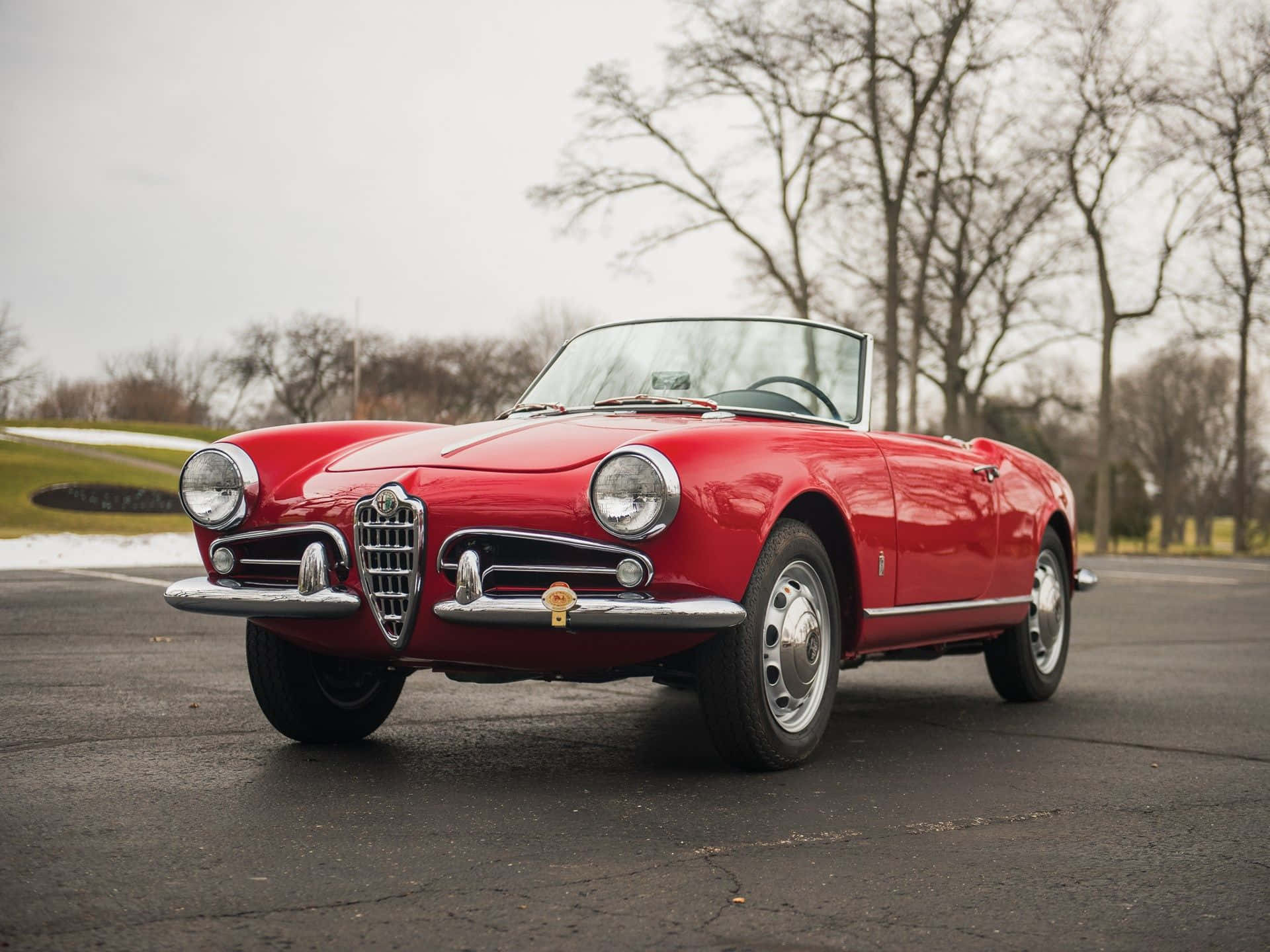 Alfa Romeo Spider 桌布 壁紙 — 一輛鮮紅色經典阿爾法羅密歐Spider敞篷車停在柏油路上，背景有光禿禿的樹木和雪堆。