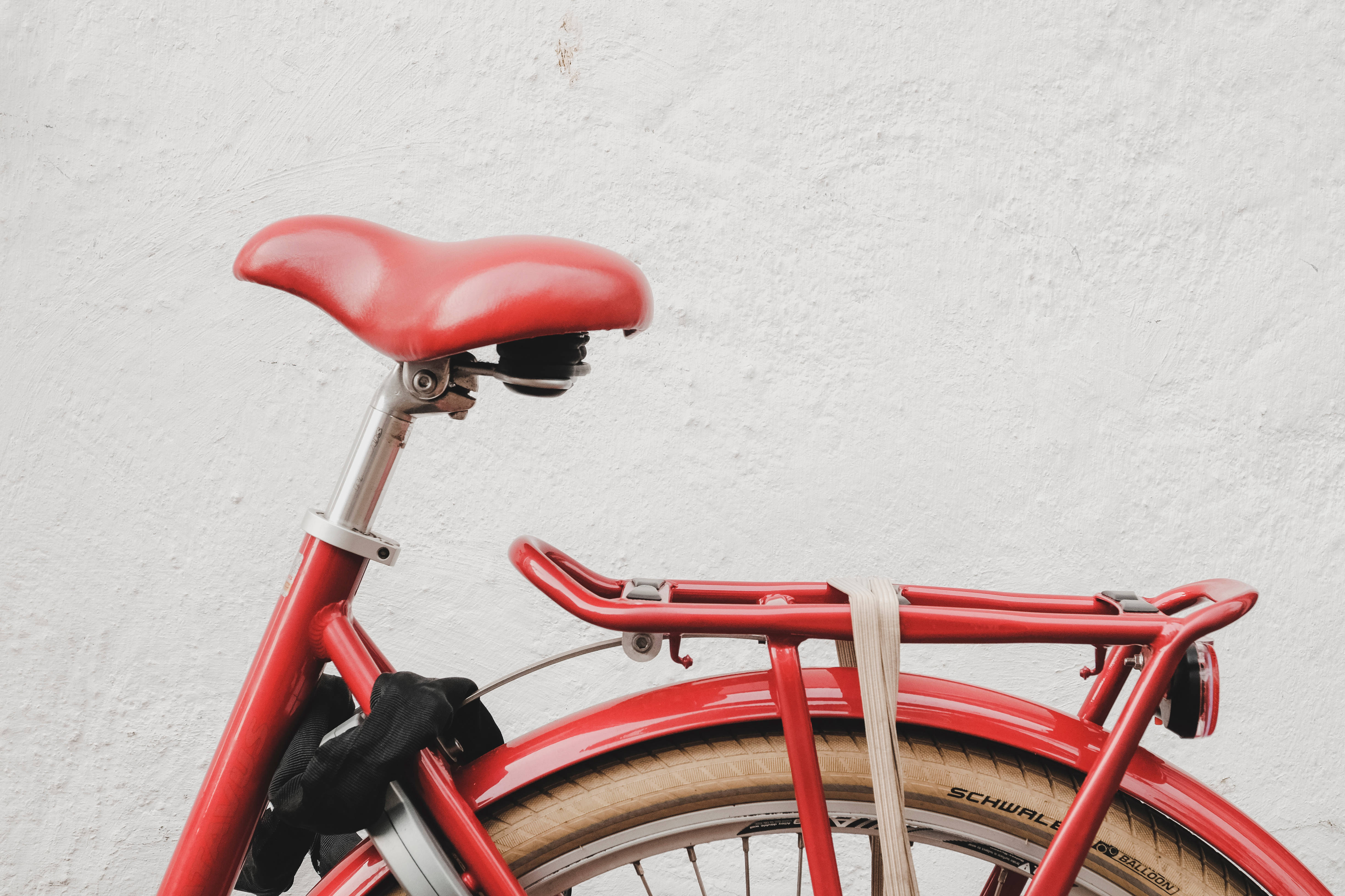 Bicycle 桌布 壁紙 — 一輛鮮紅色腳踏車的特寫，配有相配的座椅和行李架，背景是帶紋理的白色牆壁。