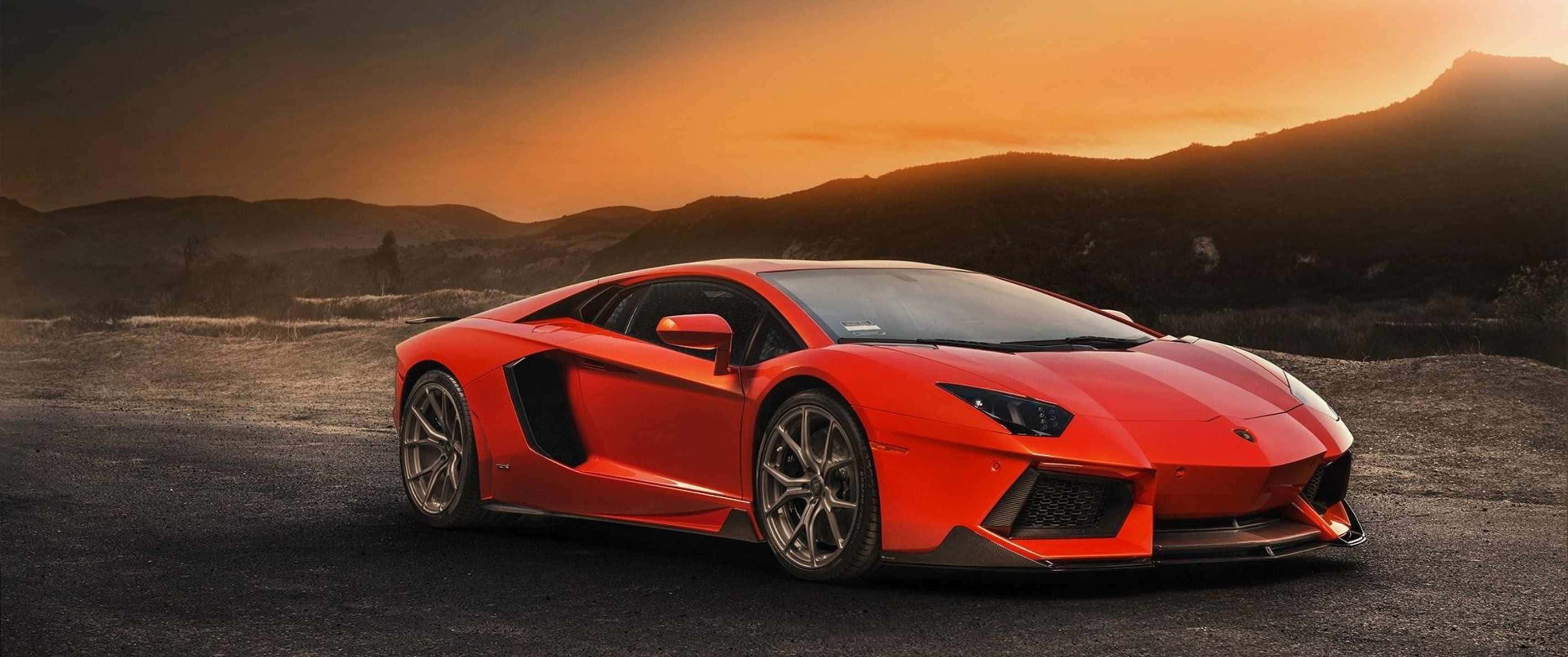 3440x1440p Lamborghini 桌布 壁紙 — 一輛鮮紅色藍寶堅尼Aventador在日落時分停泊在碎石路上，背景有山巒。