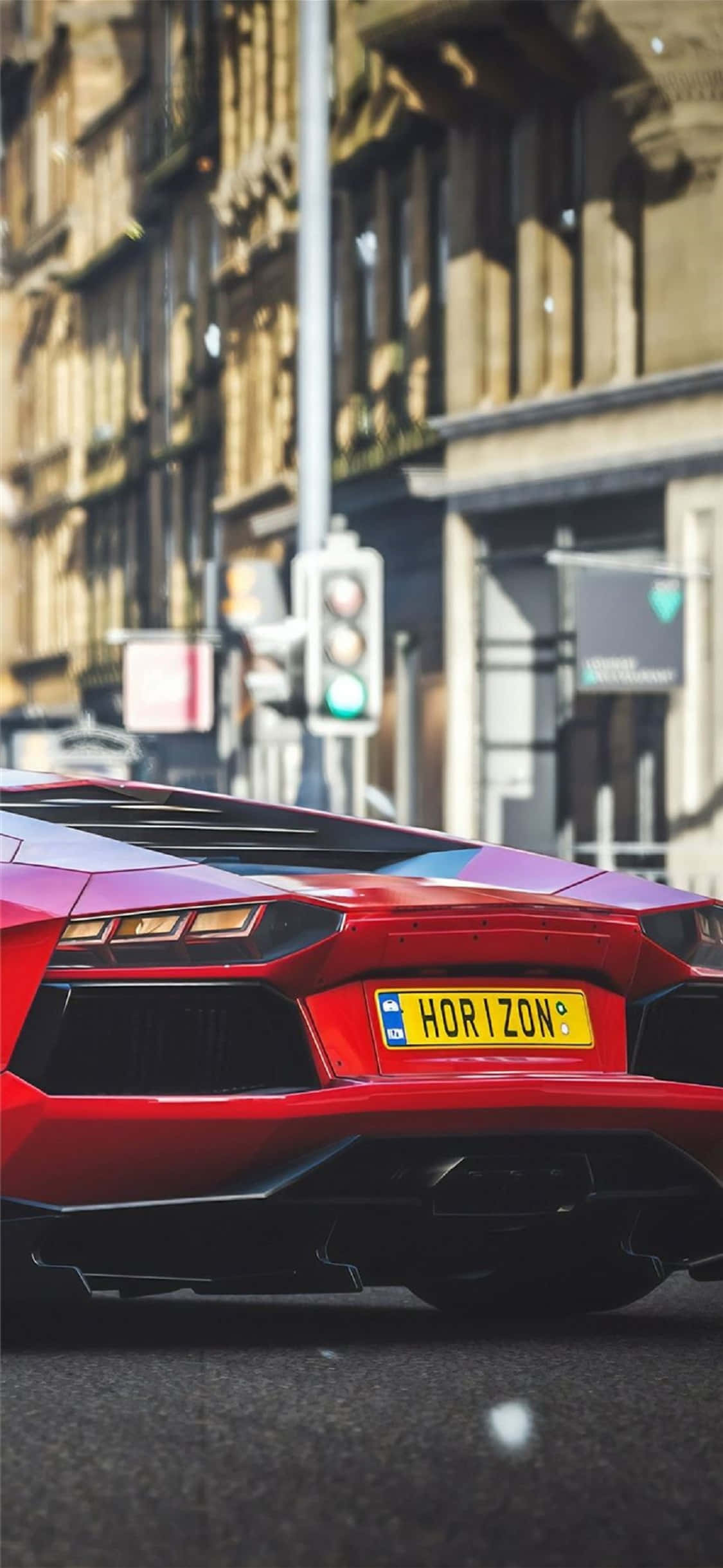 iPhone X Forza Horizon 4 桌布 壁紙 — 一輛鮮紅色藍寶堅尼Huracán的車尾視圖，停泊在陽光明媚的城市街道上，背景是柔和焦點的歷史建築。