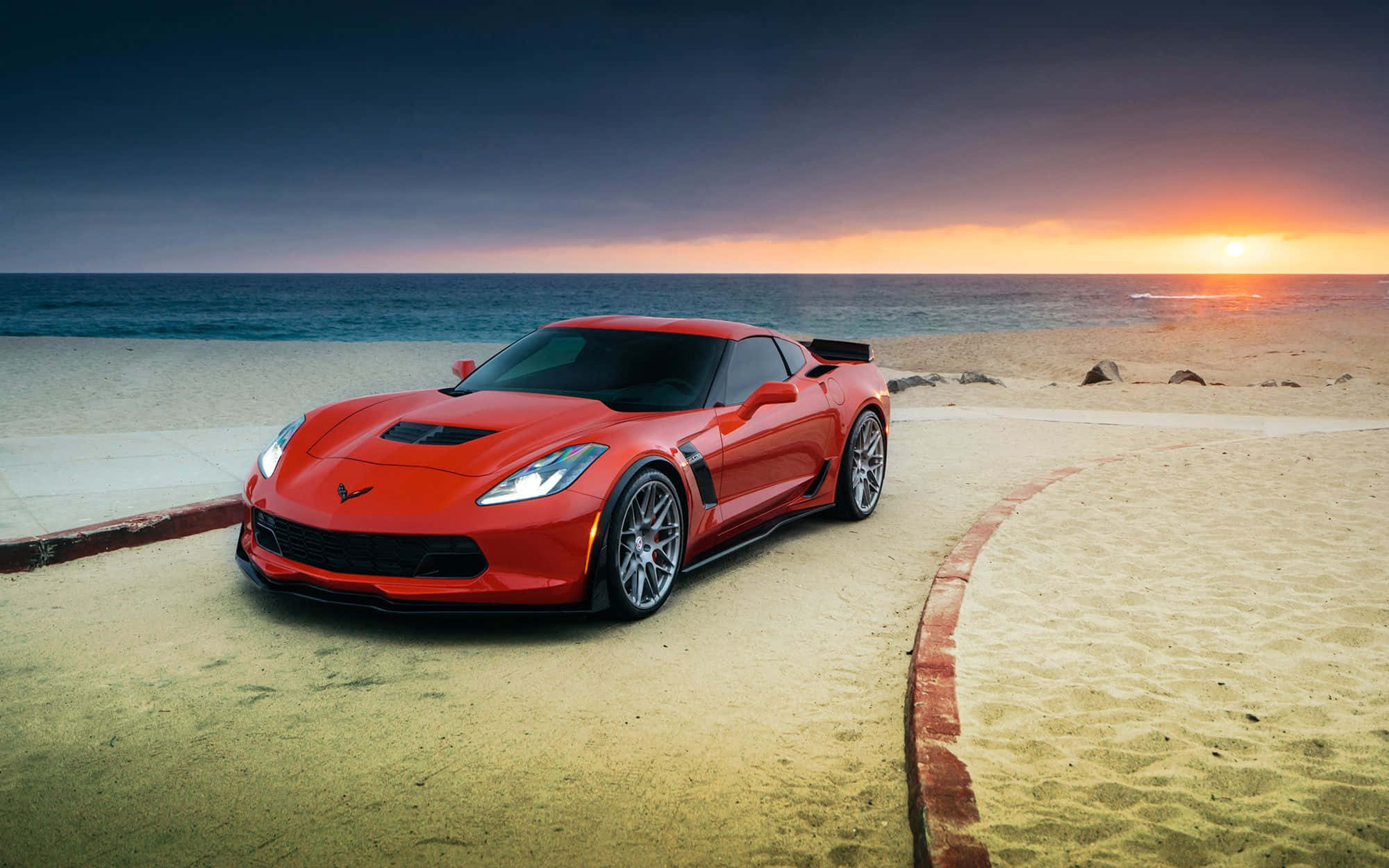 Chevrolet Corvette Z06 桌布 壁紙 — 一輛鮮紅色跑車停泊在沙灘上，背景是日落時分的海浪。