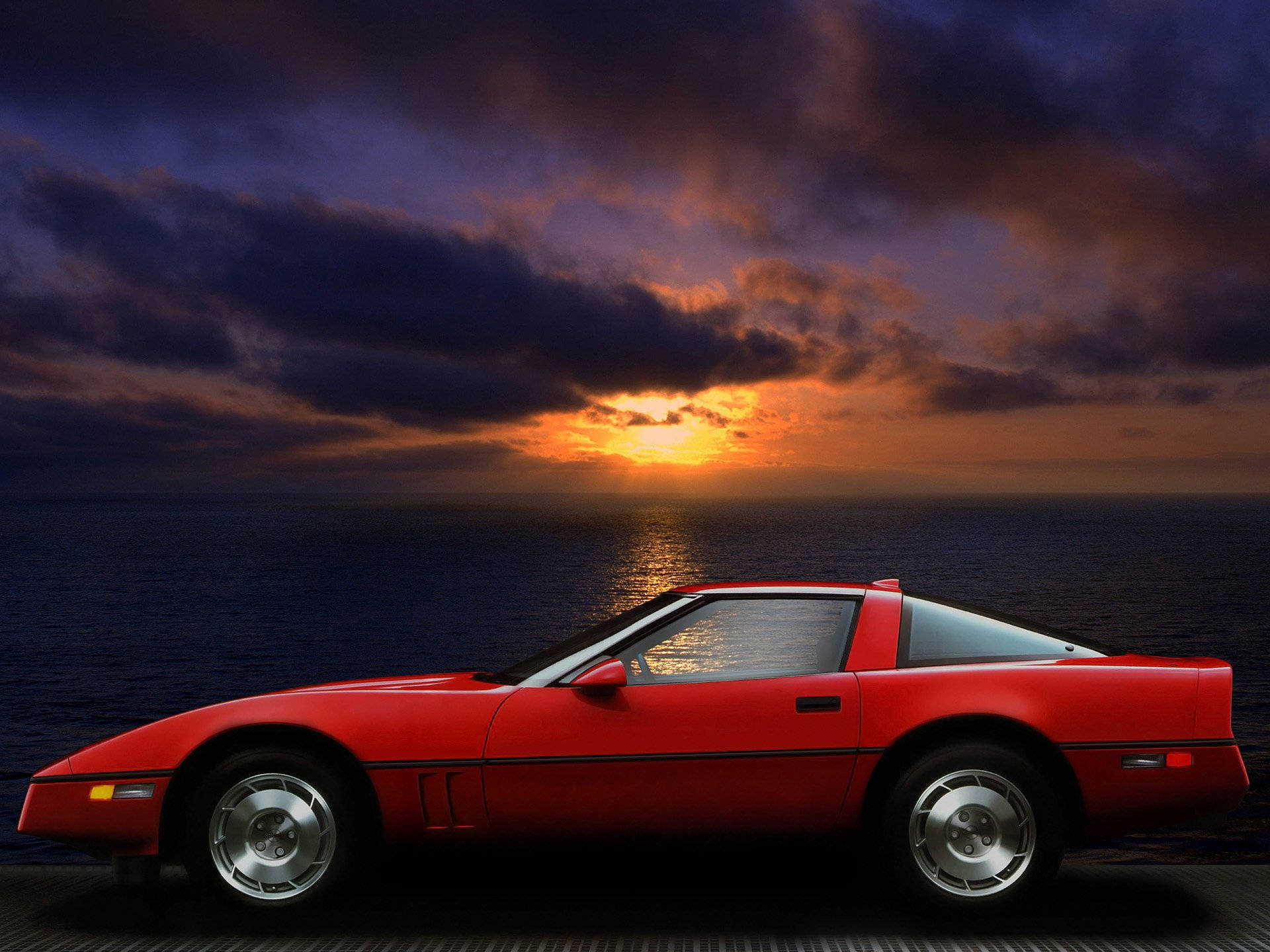corvette 桌布 壁紙 — 一輛鮮紅色跑車停泊在碼頭上，熾熱的夕陽染紅了天空，並在海面上反射。