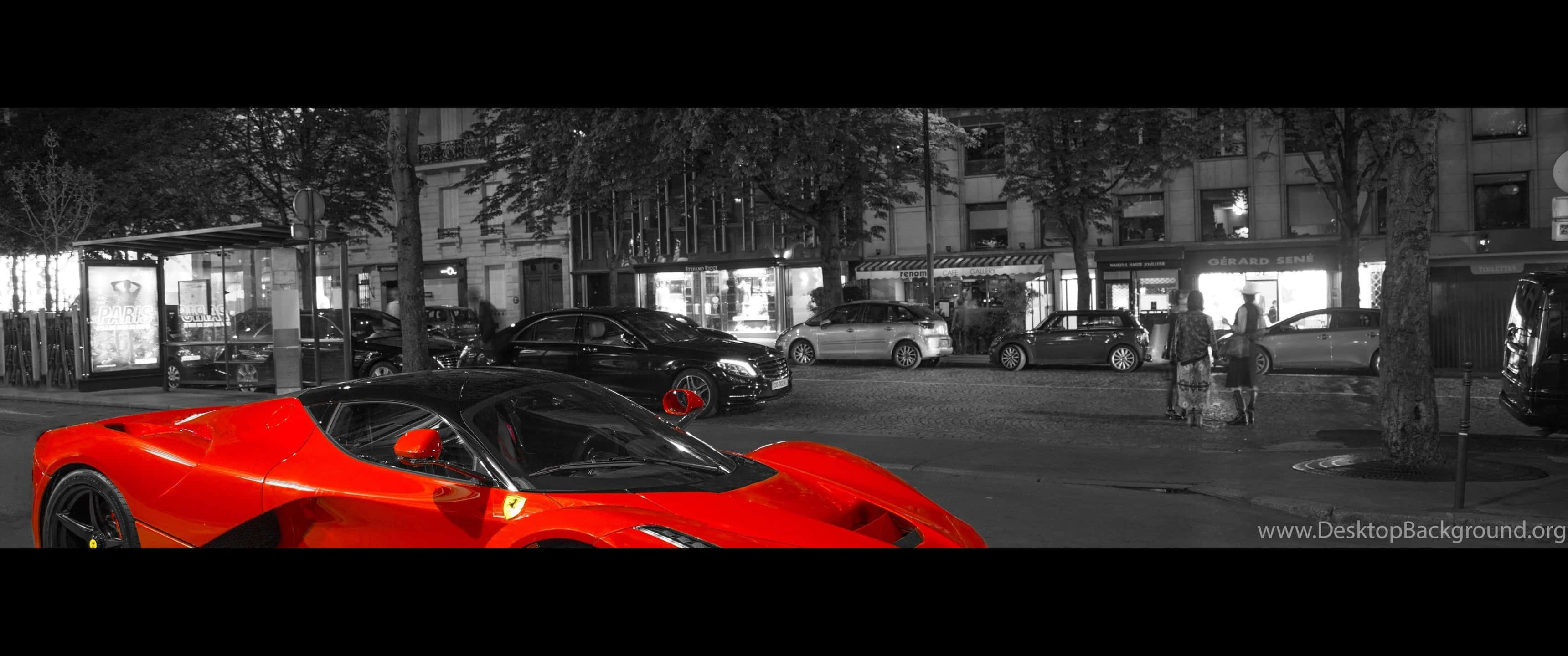 3440x1440p Ferrari 桌布 壁紙 — 一輛鮮紅色跑車在夜晚的黑白城市街道上脫穎而出，背景有行人和商店門面。