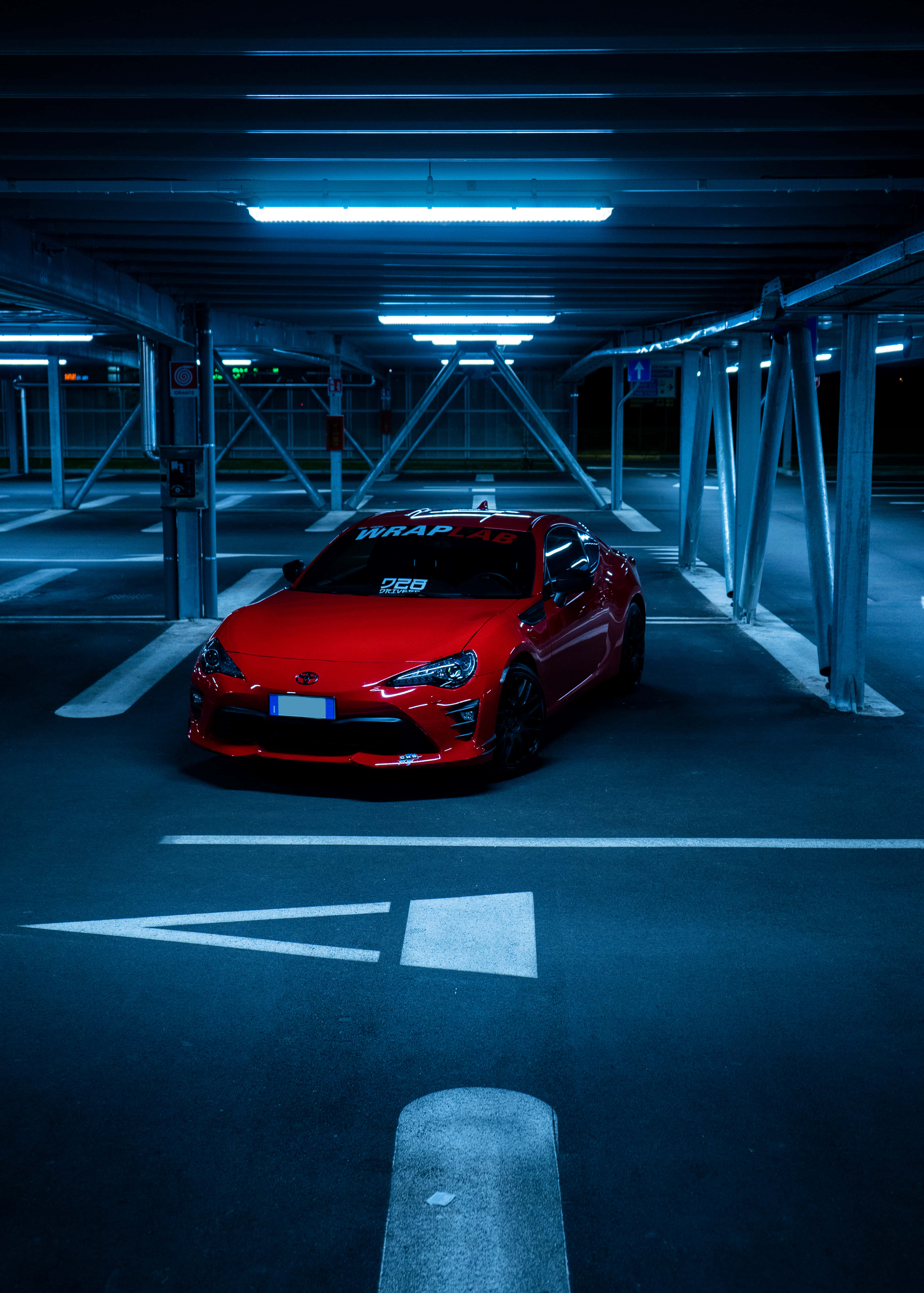桌布 壁紙 — 一輛鮮紅色跑車在夜晚空無一人的地下停車場中，在清涼的藍色螢光燈下閃閃發光。