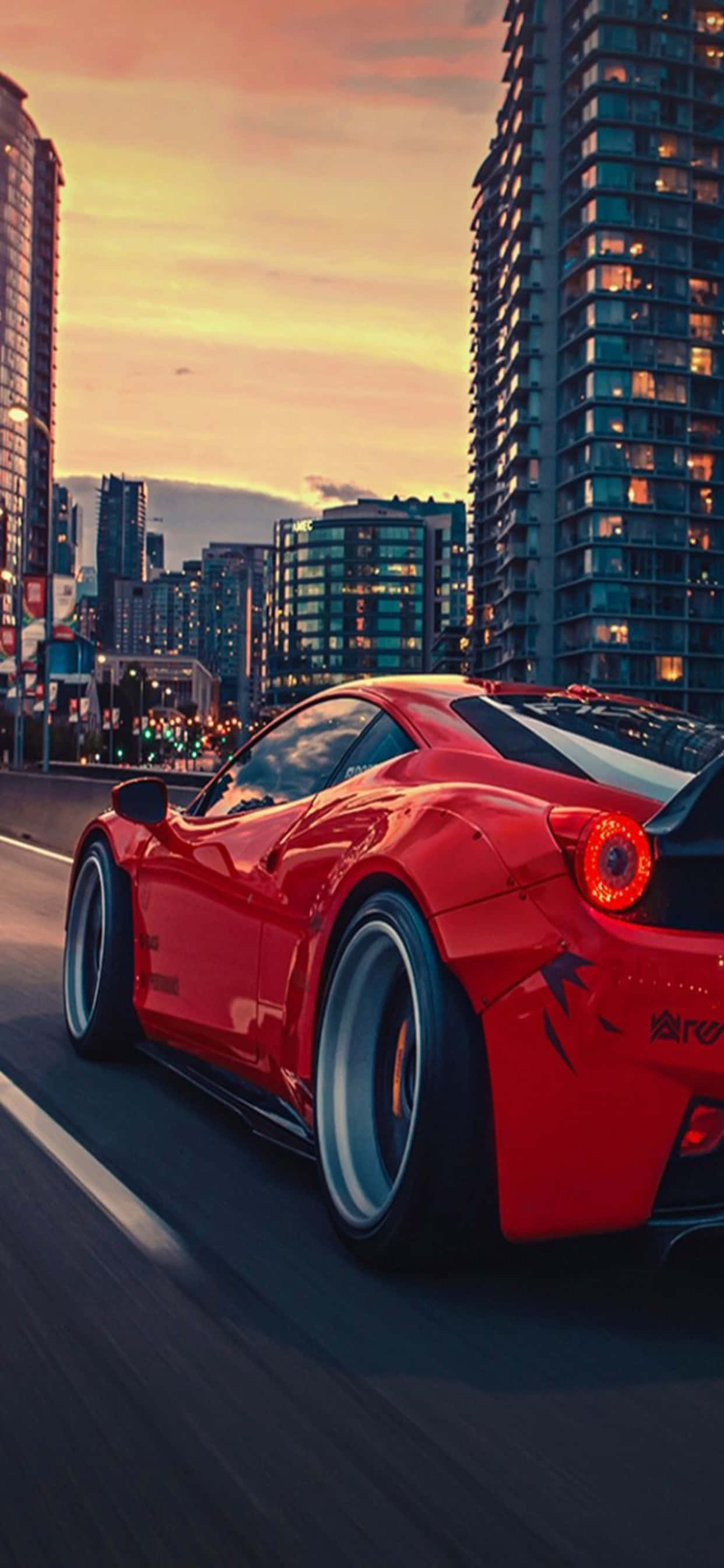 speeding car 桌布 壁紙 — 一輛鮮紅色跑車在日落時分疾馳穿過城市景觀，背景中高樓大廈閃閃發光。