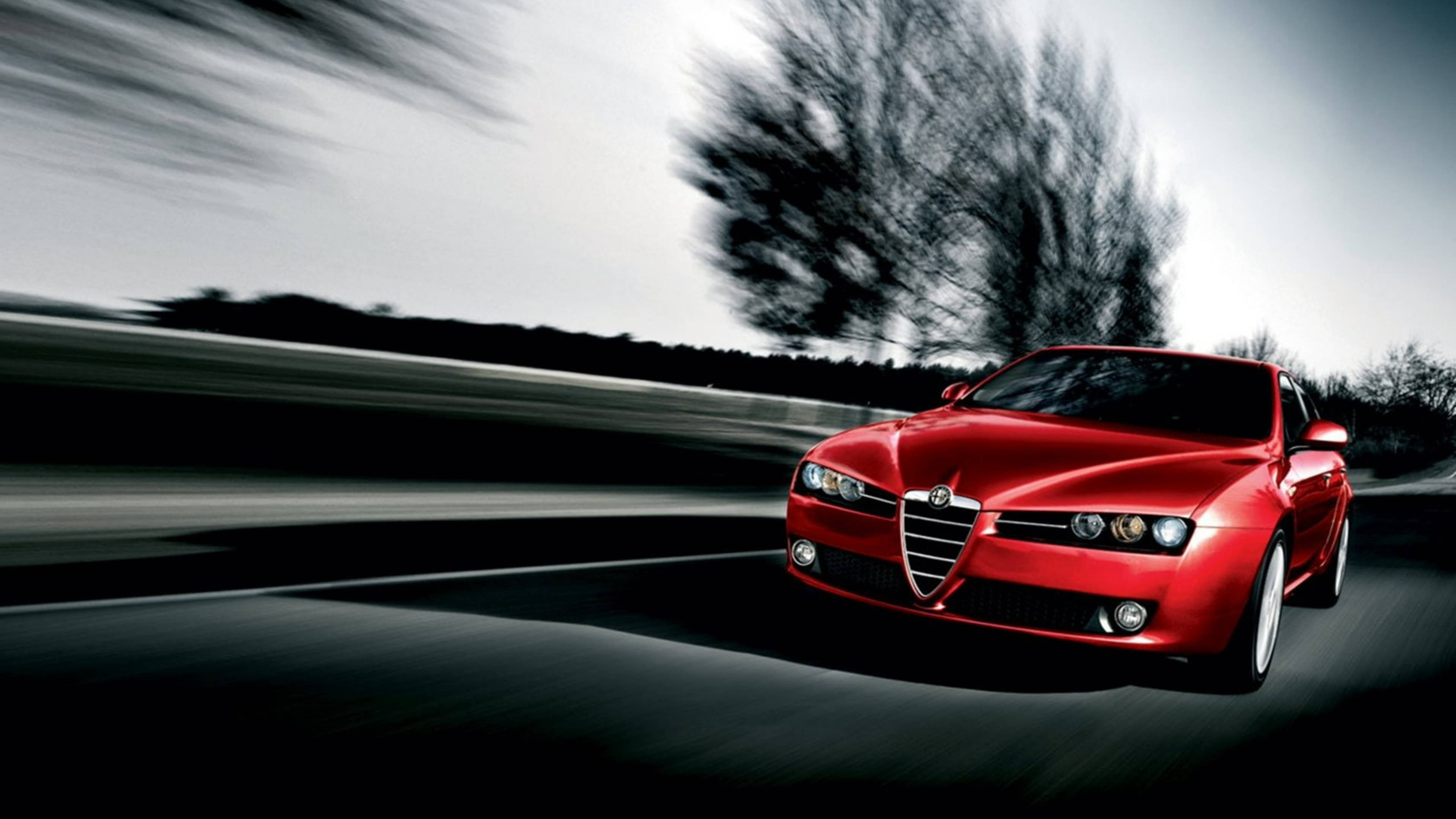 愛快羅密歐 桌布 壁紙 — 一輛鮮紅色跑車在模糊的道路上疾馳，背景有動態模糊的樹木。