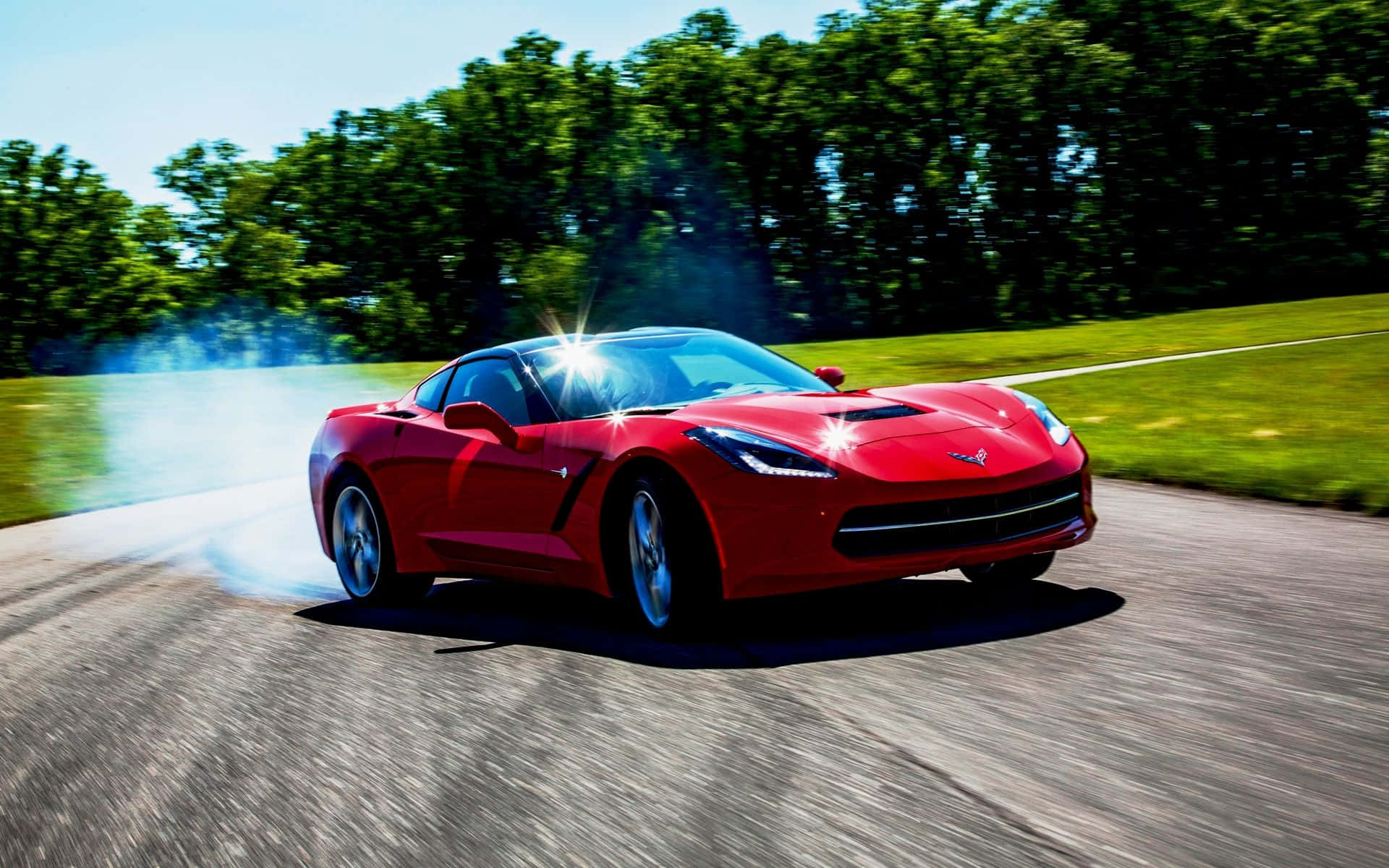 Chevrolet Corvette Stingray 桌布 壁紙 — 一輛鮮紅色跑車在陽光照耀的彎道上飄移，背景是茂密的綠樹。