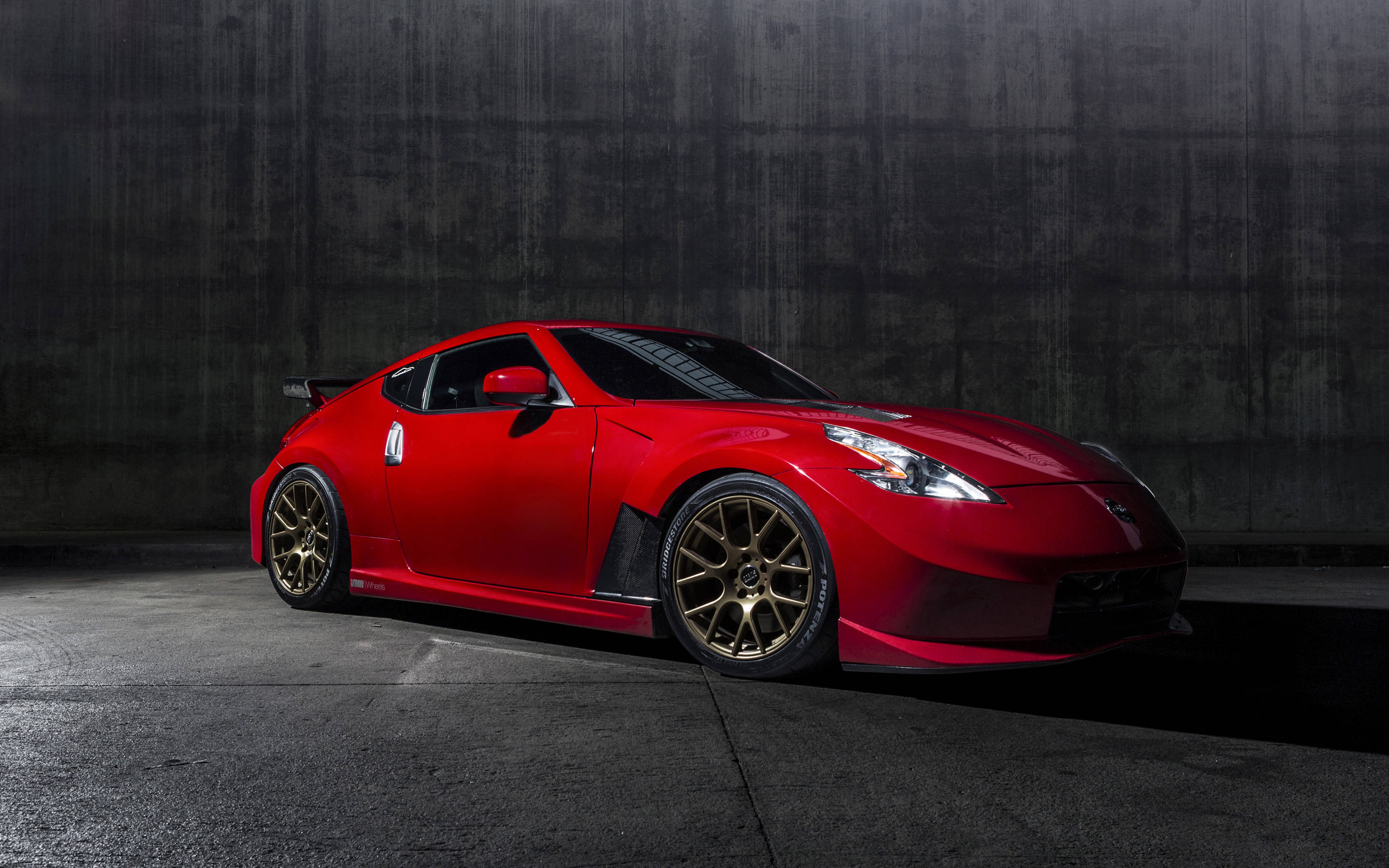 Nissan 370z 桌布 壁紙 — 一輛鮮紅色跑車配金色輪圈，在昏暗車庫中戲劇性地照亮，背景是深色混凝土牆。