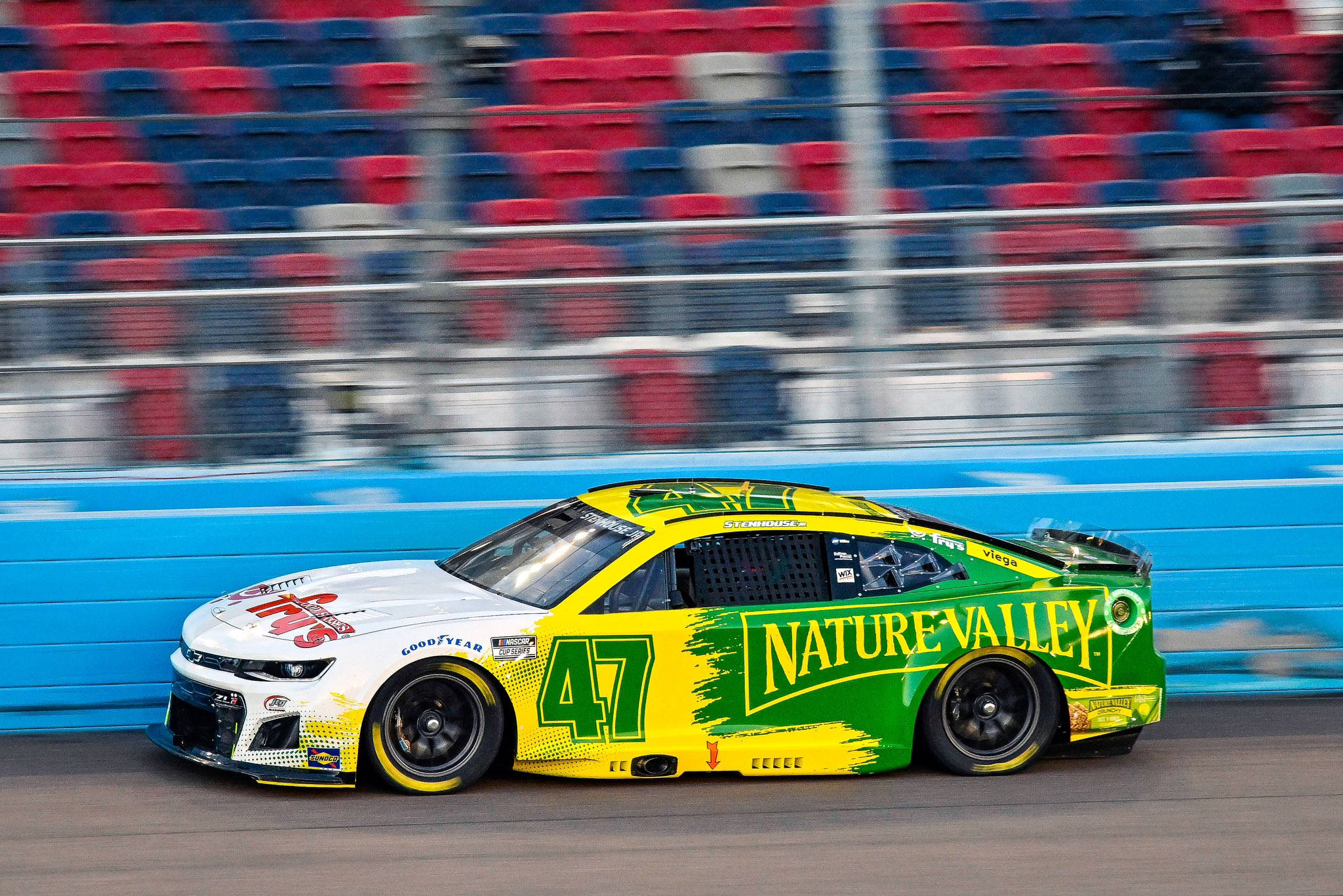 Racing 桌布 壁紙 — 一輛鮮綠色和黃色的NASCAR賽車（47號）在模糊的紅色和藍色體育場座位旁疾馳而過。