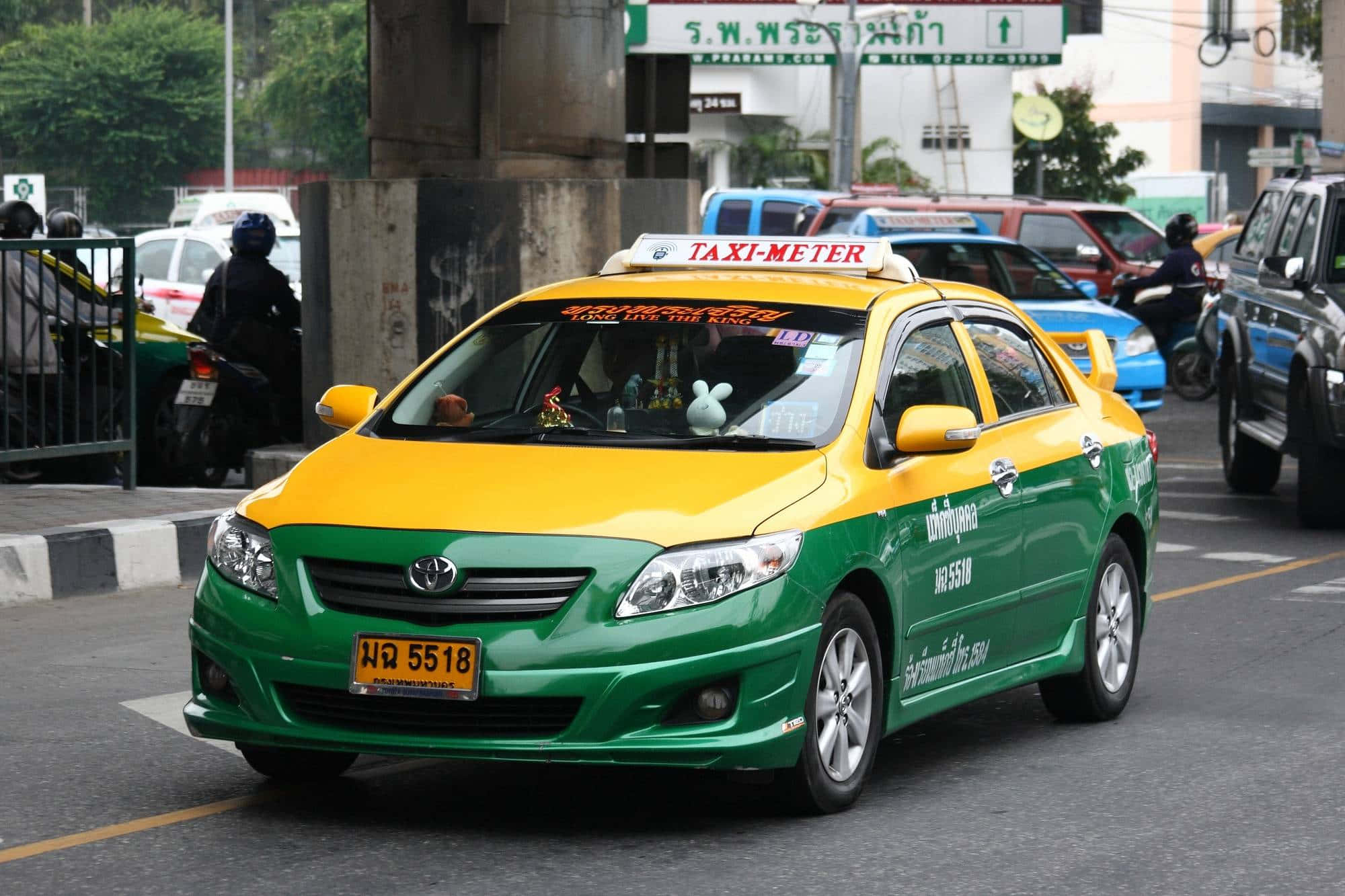 taxi 桌布 壁紙 — 一輛鮮綠色和黃色的計程車在曼谷繁忙的街道上行駛，背景有其他車輛和摩托車。