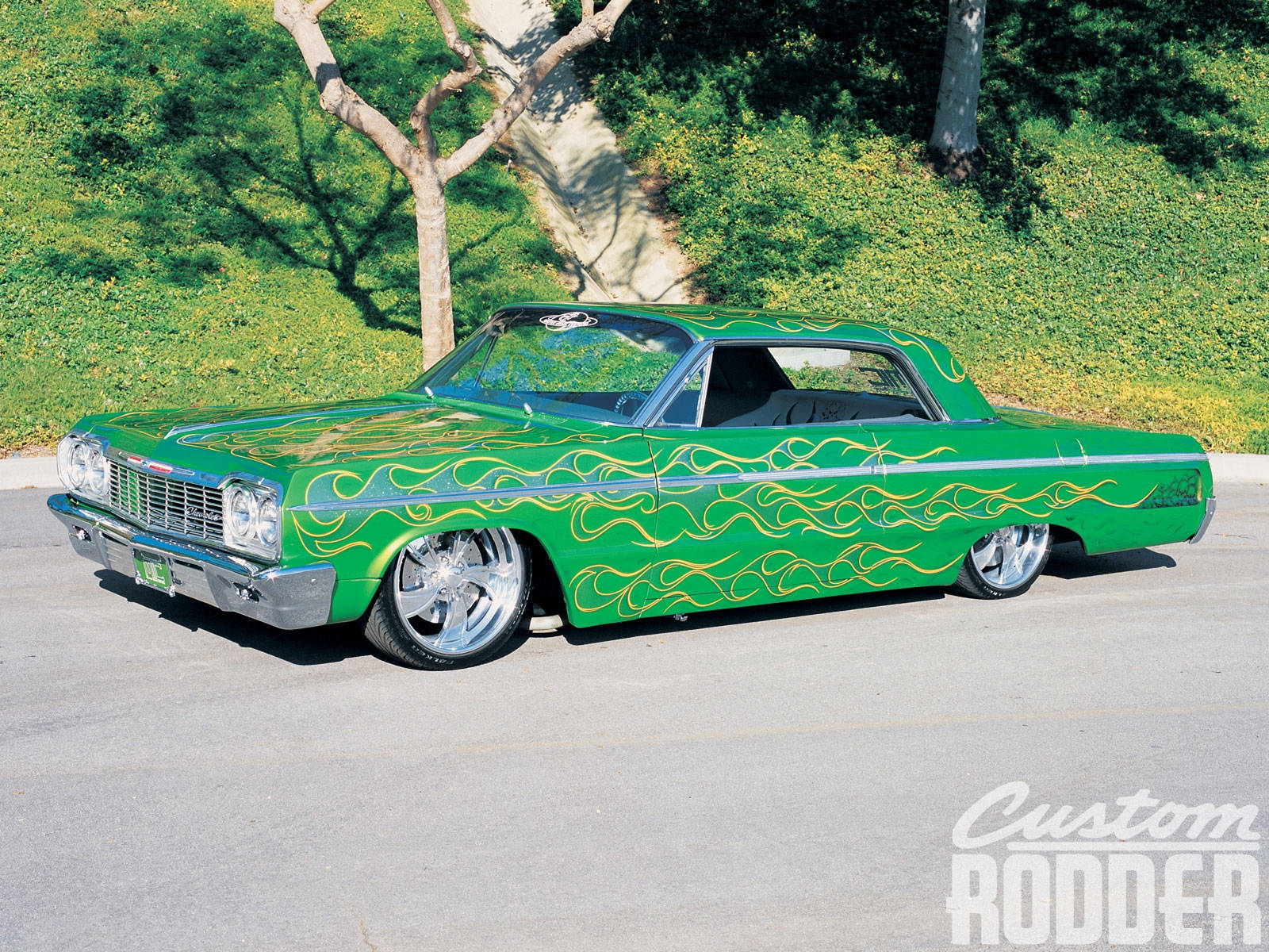 Lowrider 桌布 壁紙 — 一輛鮮綠色定制車帶有黃色火焰貼紙，停在柏油路上，旁邊是草地山坡，陽光普照。
