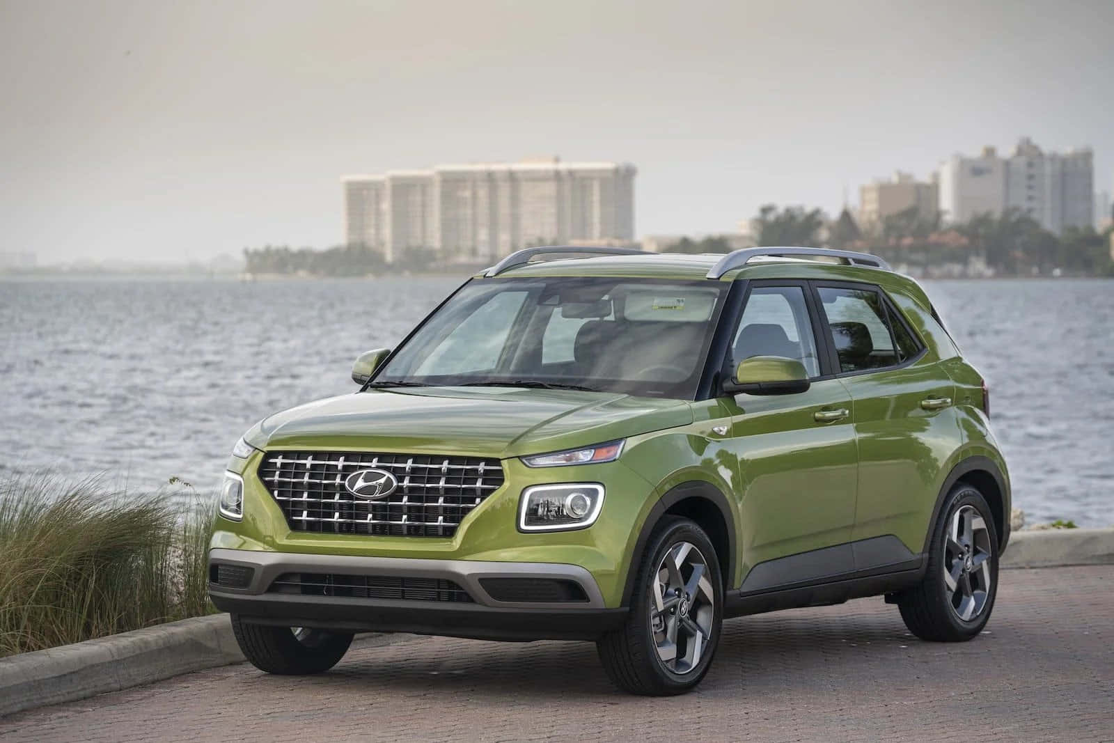 Hyundai 桌布 壁紙 — 一輛鮮綠色現代SUV停在海濱，遠處朦朧的城市建築。