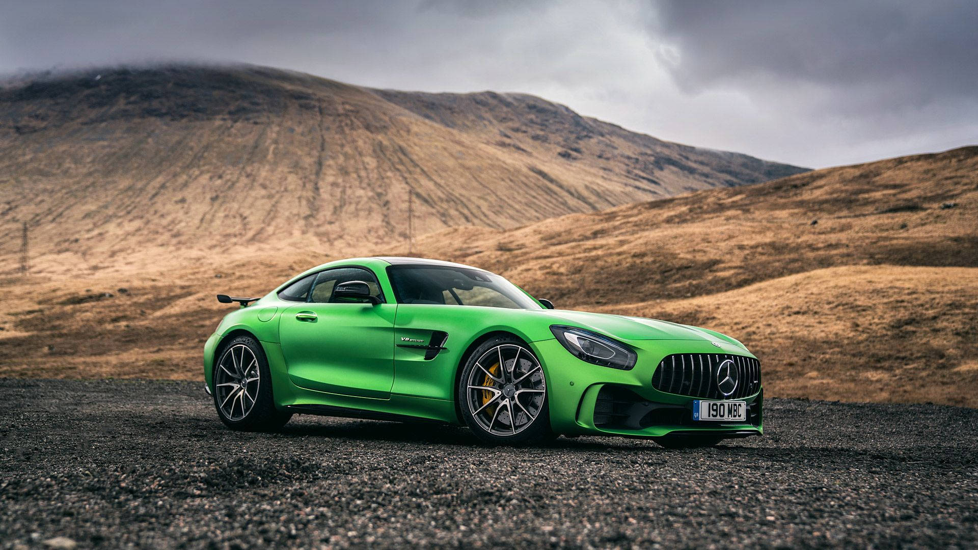 Mercedes 桌布 壁紙 — 一輛鮮綠色的 Mercedes-AMG GT 停在碎石路上，背景是荒蕪的山丘和陰天。