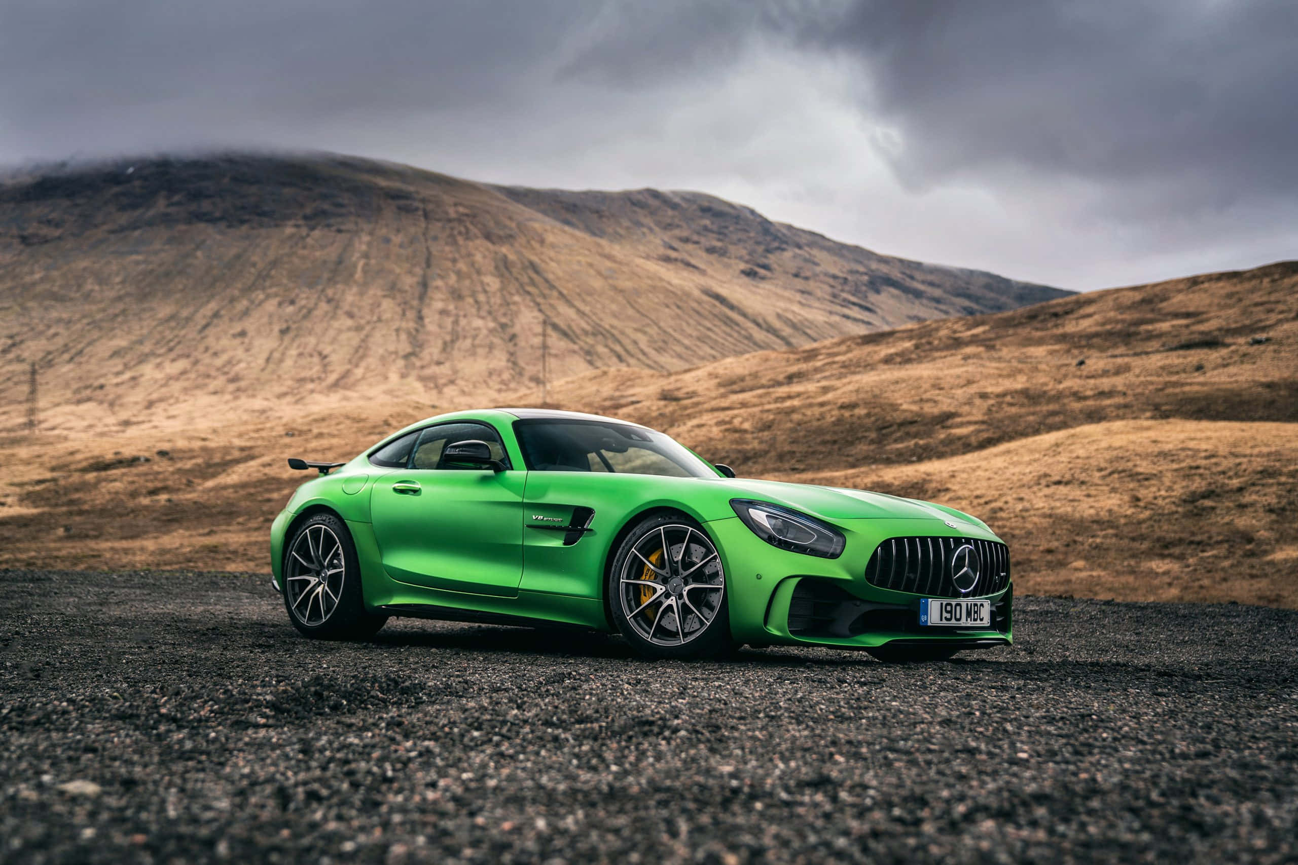 Mercedes 桌布 壁紙 — 一輛鮮綠色賓士AMG GT跑車停在碎石上，背景是戲劇性的多雲天空和荒蕪的山丘。