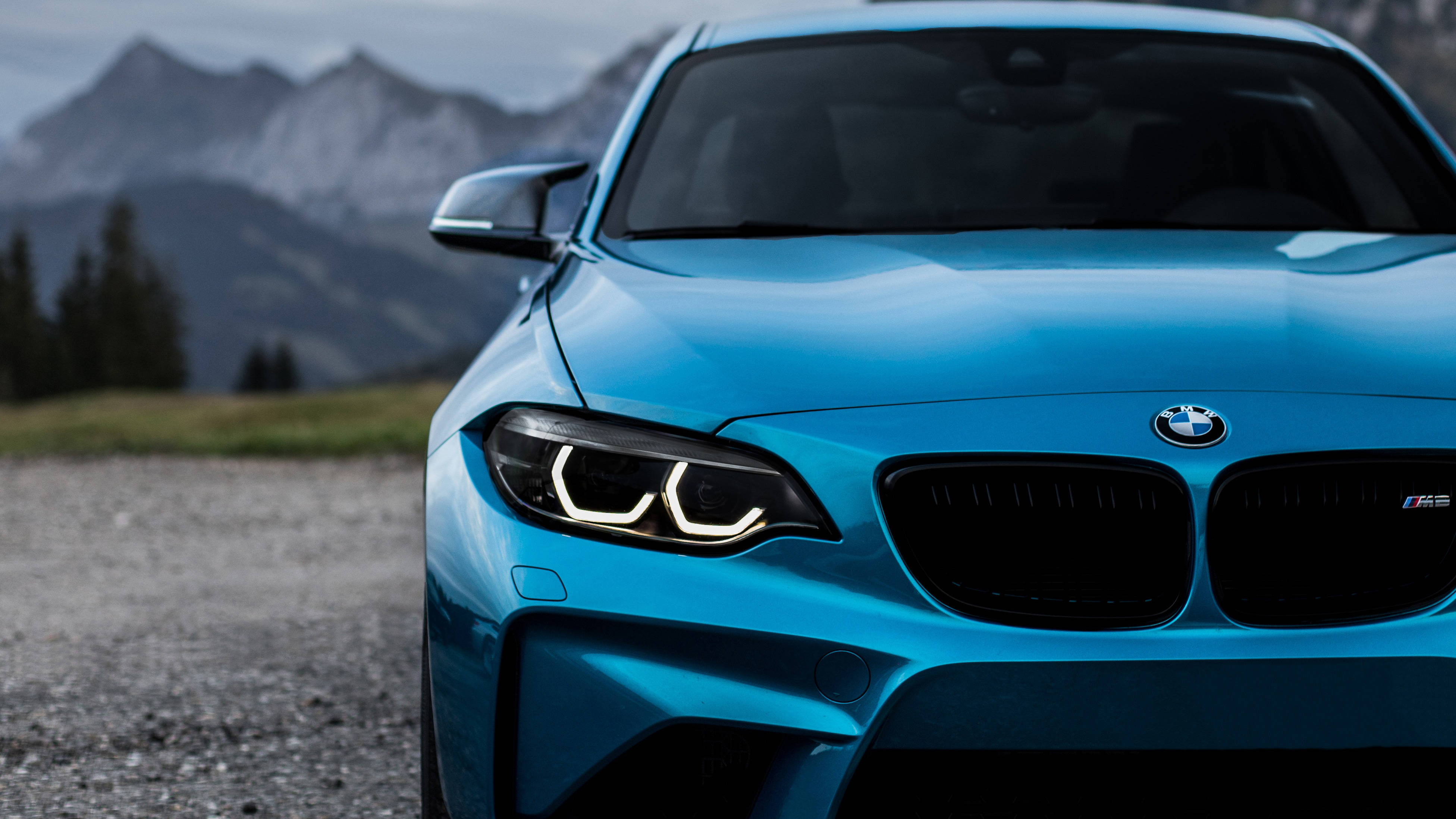 4K BMW 壁紙 桌布 壁紙 — 一輛鮮藍色BMW M2跑車停泊在碎石路上，背景是霧氣瀰漫的雪山。