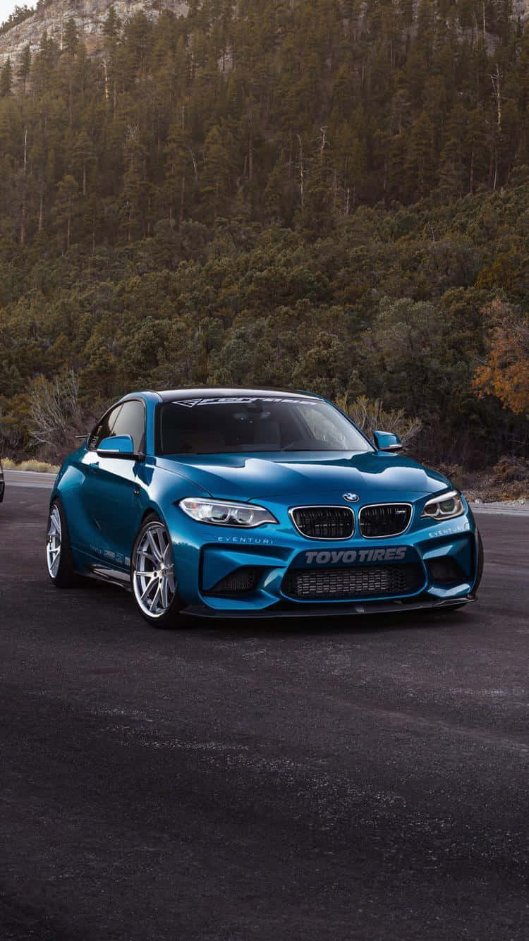 BMW 動圖 桌布 壁紙 — 一輛鮮藍色BMW M2雙門跑車帶有Toyo Tires品牌標誌，停在黑暗的瀝青路上，背景是茂密的森林山丘。