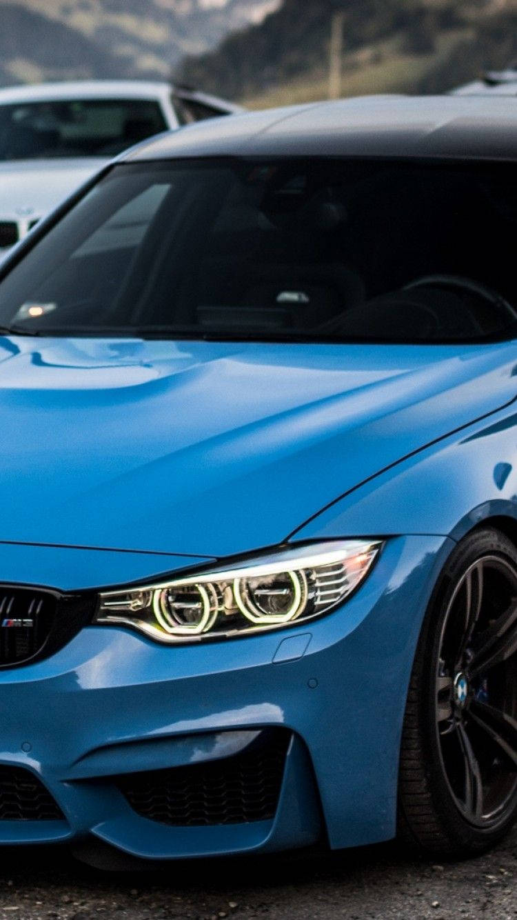 iPhone 桌布 壁紙 — 一輛鮮藍色BMW M4跑車，帶有發光頭燈，停放在戶外，背景是山巒。