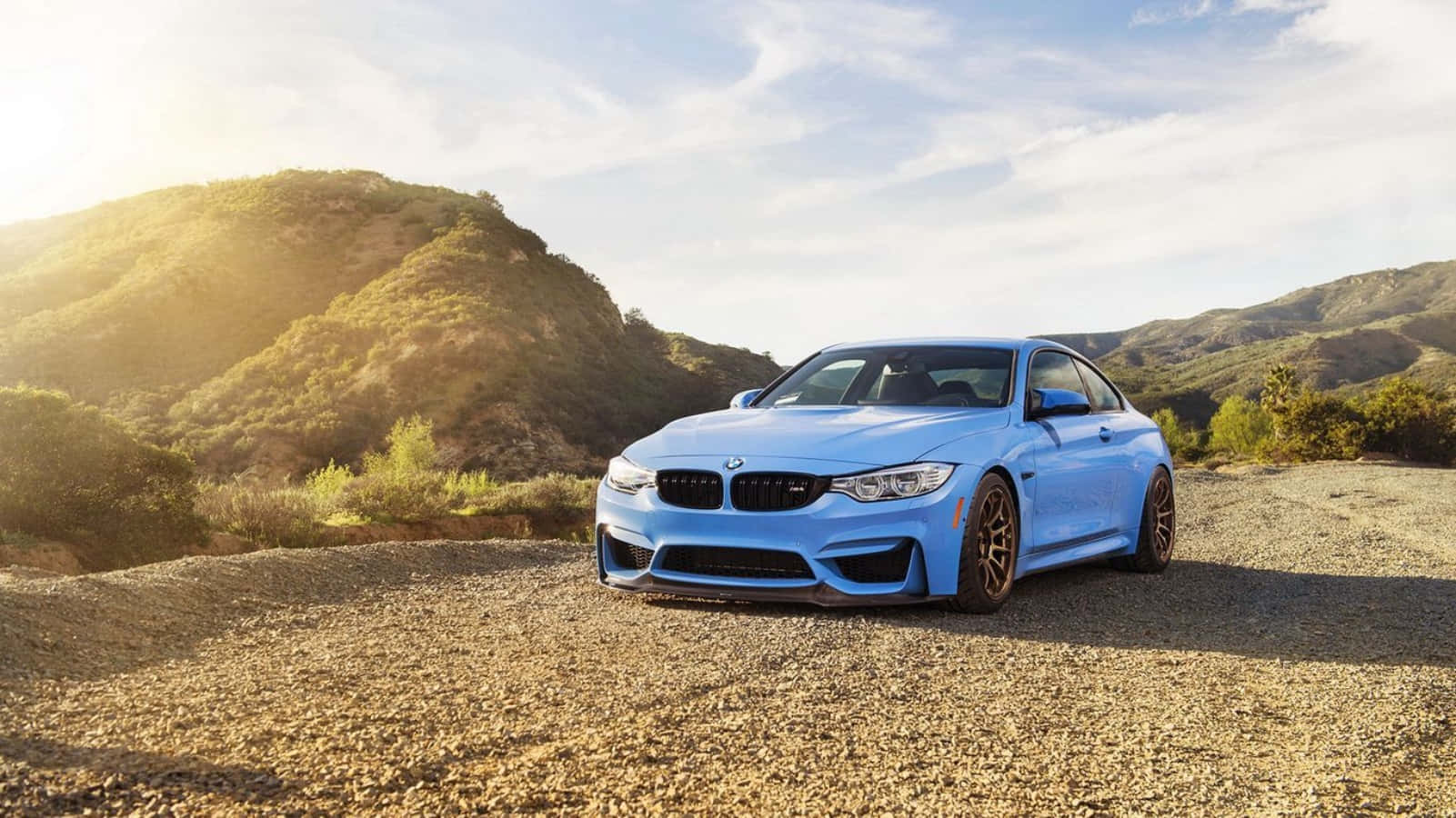 Bmw M4 桌布 壁紙 — 一輛鮮藍色BMW M4雙門跑車停泊在陽光明媚的碎石路上，背景是起伏的綠色山丘。