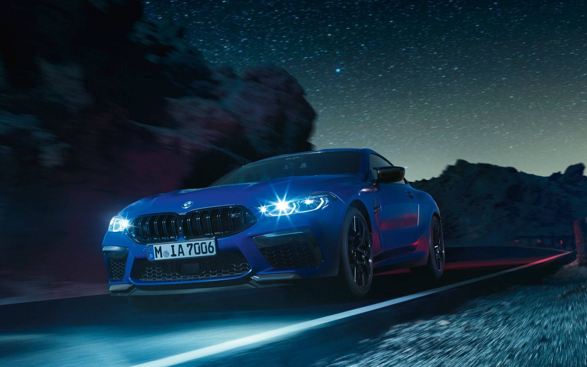夜空 桌布 壁紙 — 一輛鮮藍色BMW M8 Coupe在繁星點點的夜空下，沿著蜿蜒的山路疾馳，明亮的車頭燈劃破黑暗。