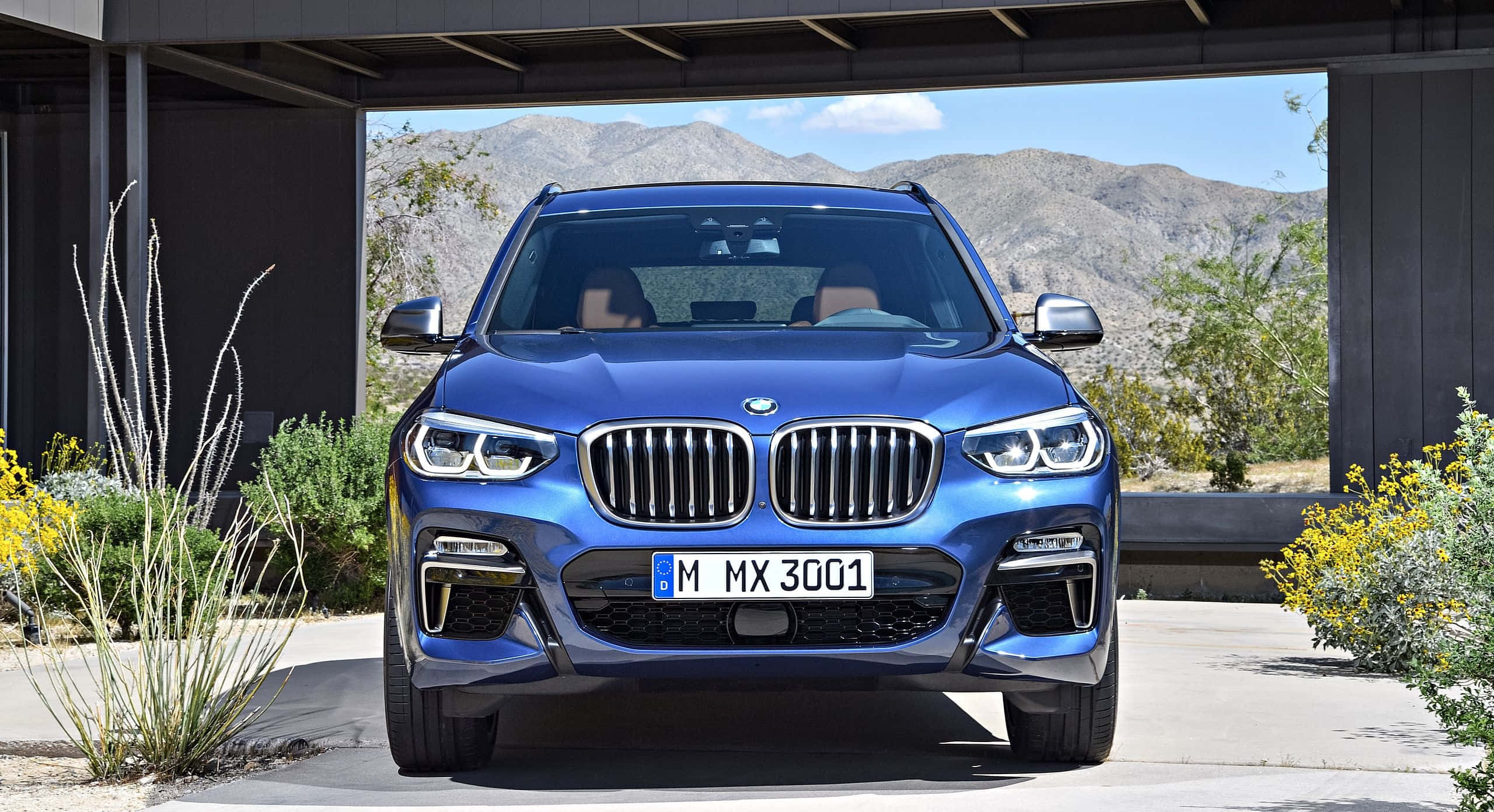 Bmw X3 桌布 壁紙 — 一輛鮮藍色BMW X3 SUV停放在現代車棚下，背景有沙漠山脈和黃色花朵。