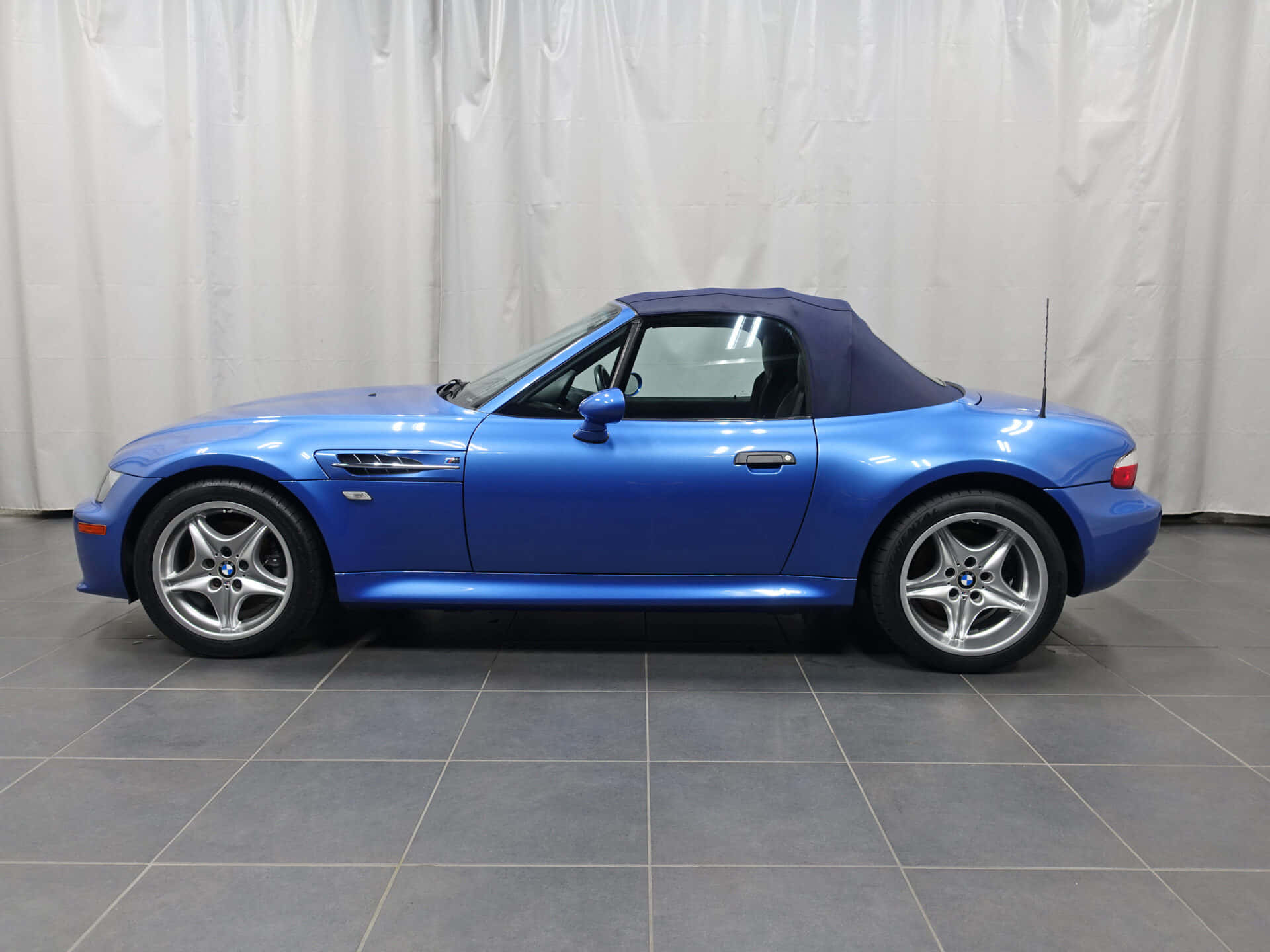 Bmw Z3 桌布 壁紙 — 一輛鮮藍色BMW Z8敞篷車，配深藍色軟頂，停放在灰色瓷磚地板上，背景為白色窗簾。