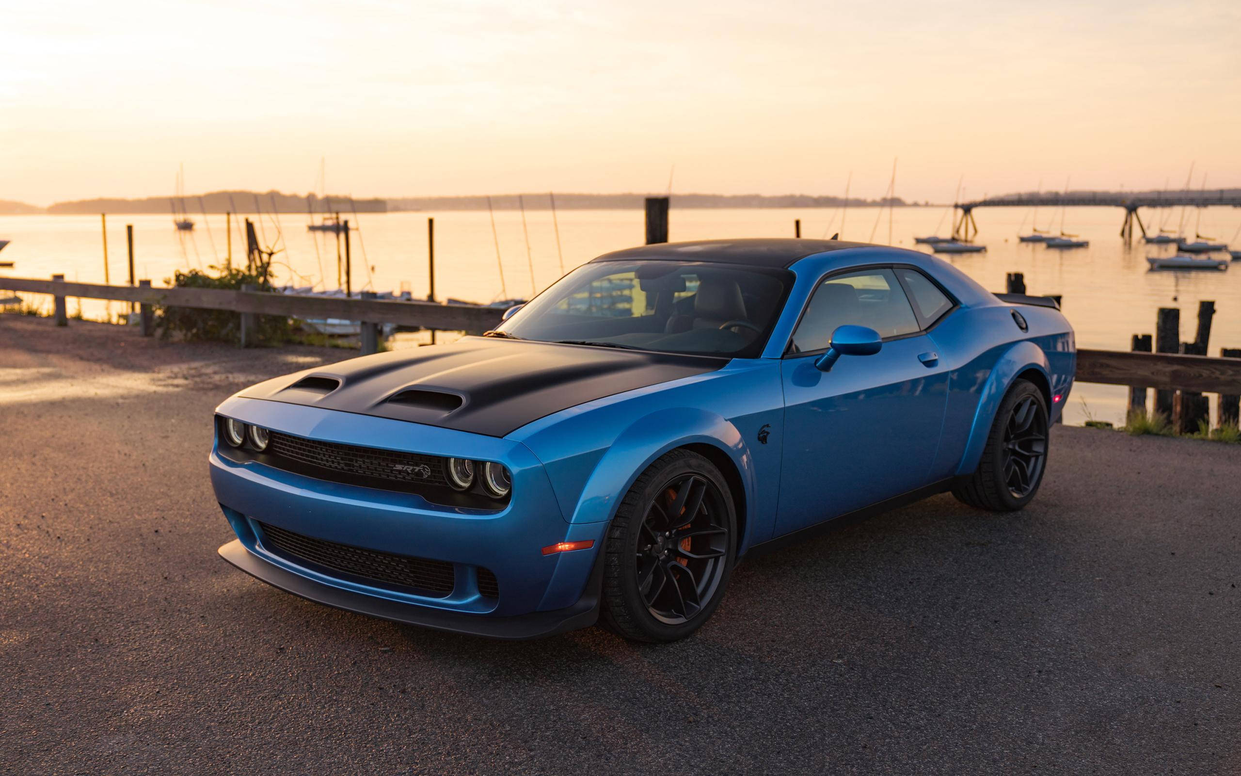 Challenger 桌布 壁紙 — 一輛鮮藍色Dodge Challenger配黑色引擎蓋，在日落時分停泊在碼頭道路上，後方平靜的水面上有船隻停泊。