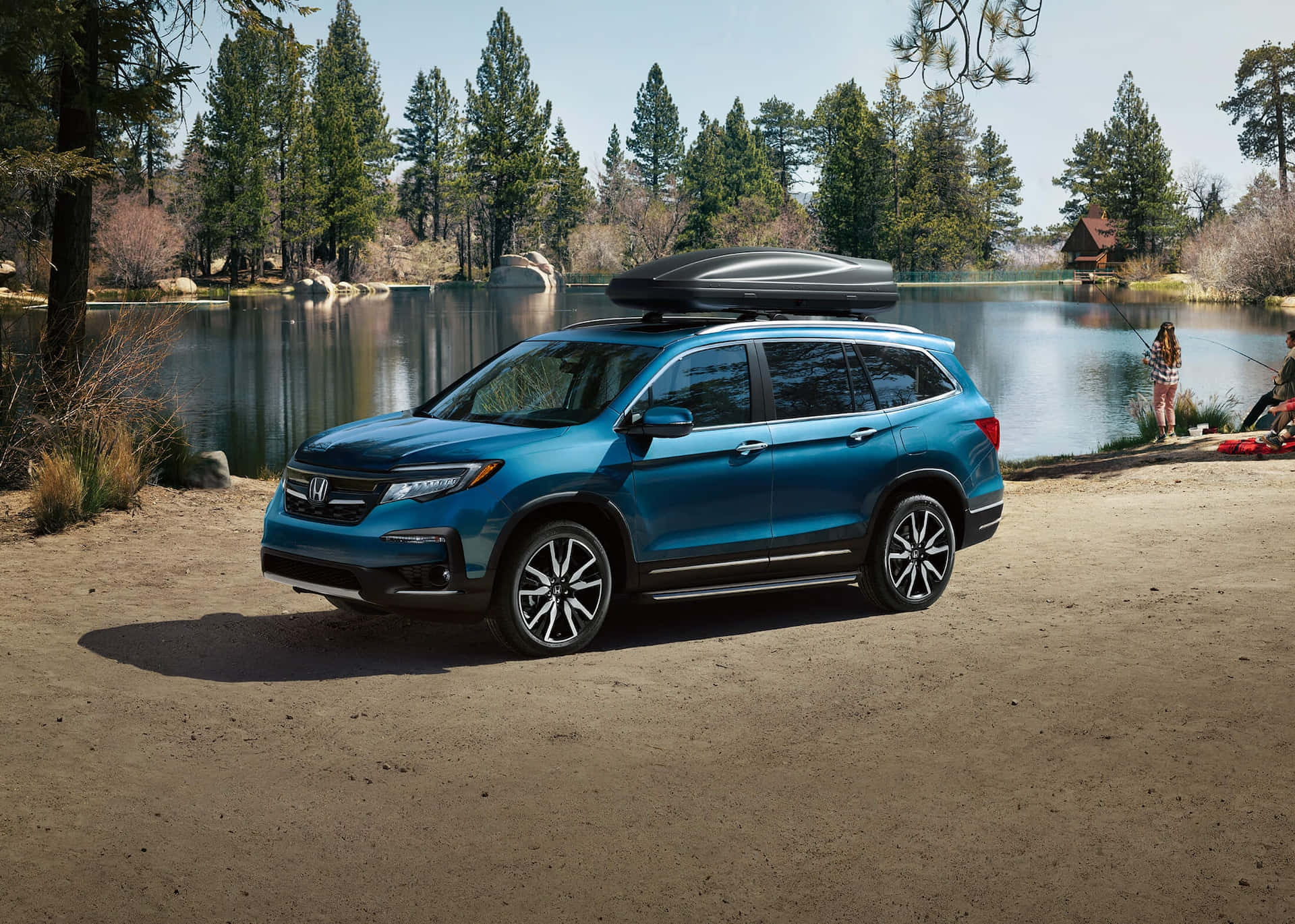Honda Pilot 桌布 壁紙 — 一輛鮮藍色SUV連車頂行李箱停泊在湖邊，周圍是高聳的松樹，天空晴朗。
