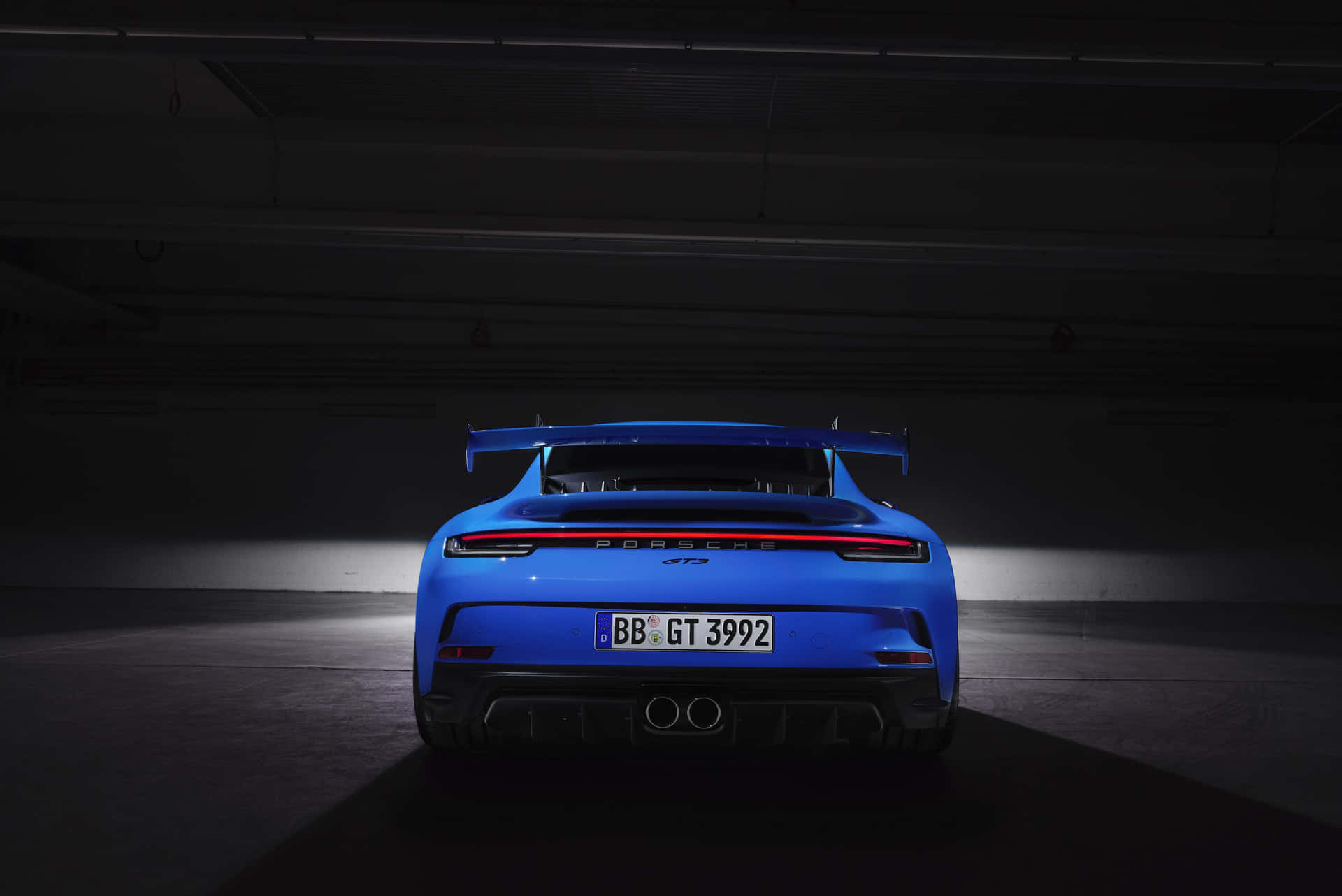 保時捷 桌布 壁紙 — 一輛鮮藍色保時捷911 GT3 RS在黑暗的地下停車場中從後方戲劇性地照亮，展示其流線型尾部設計和大尾翼。