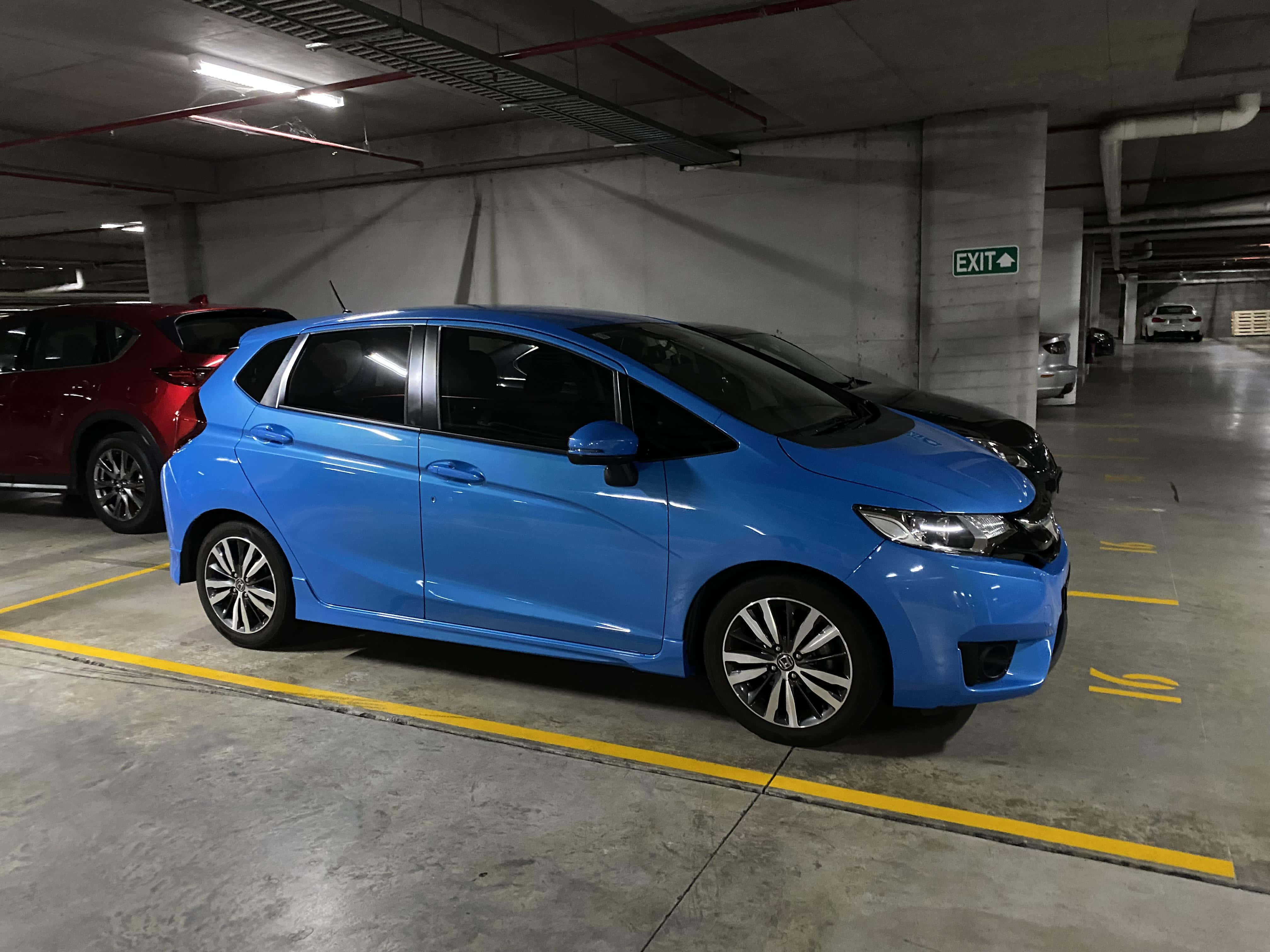Honda Fit 桌布 壁紙 — 一輛鮮藍色小型車停放在設有黃線和出口標誌的混凝土地下停車場。