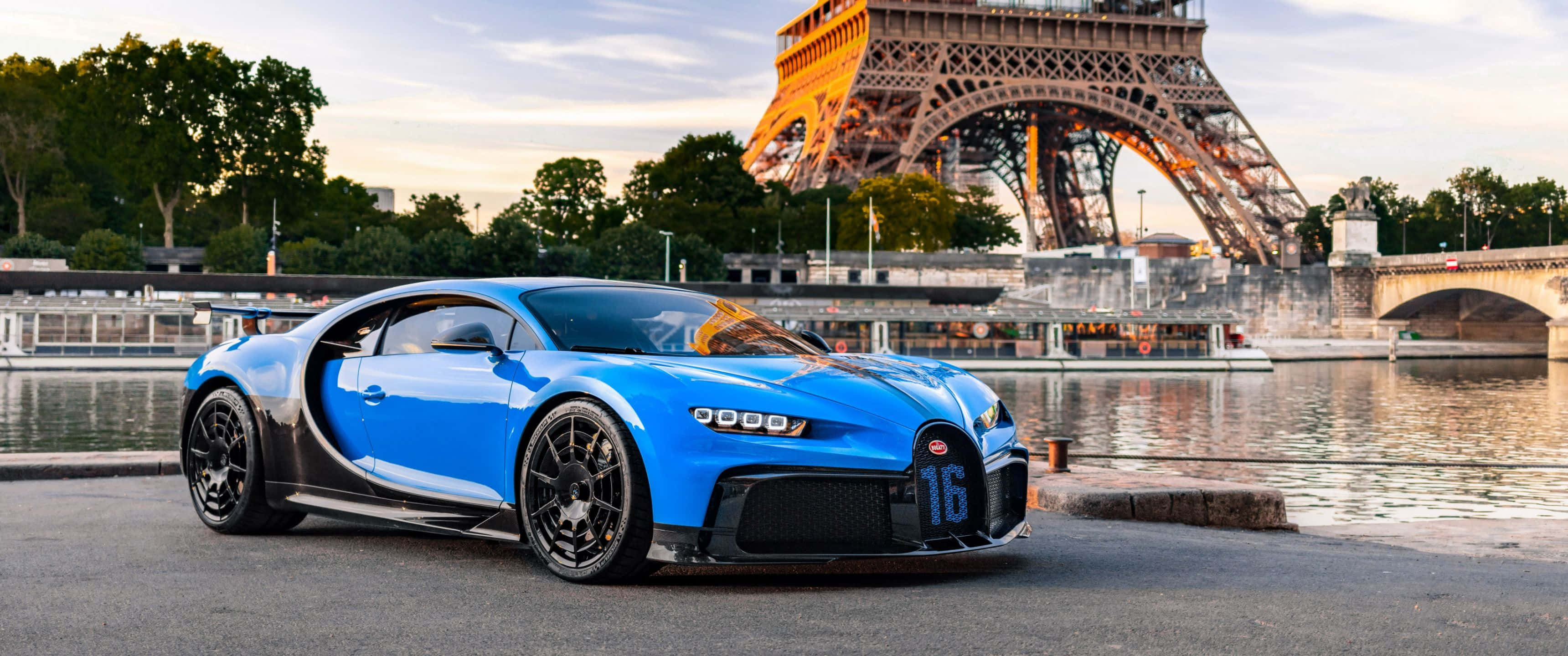 3440x1440p Bugatti 桌布 壁紙 — 一輛鮮藍色布加迪Chiron停泊在塞納河畔，背後是金色夕陽下閃耀的艾菲爾鐵塔。