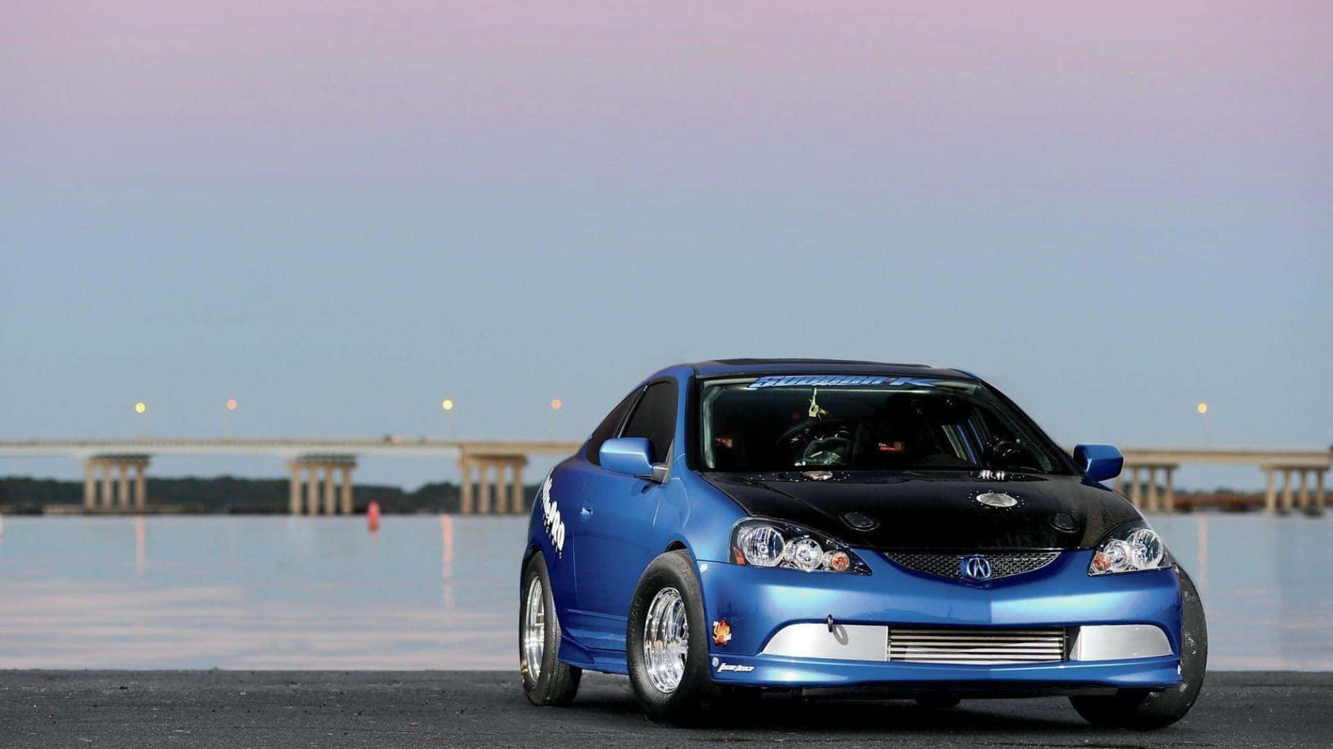 Rsx Type-s 桌布 壁紙 — 一輛鮮藍色改裝跑車，黑色引擎蓋，停泊在暮色中的海濱碼頭，背景中遠處的橋樑柔和地發光。