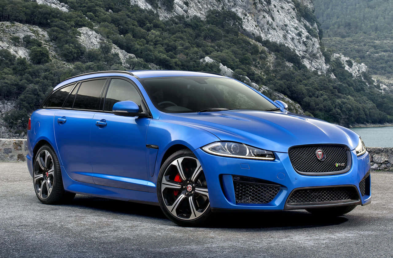Jaguar Xfr 桌布 壁紙 — 一輛鮮藍色的Jaguar XF Sportbrake停放在石頭觀景點上，背景是岩石山脈和綠意。