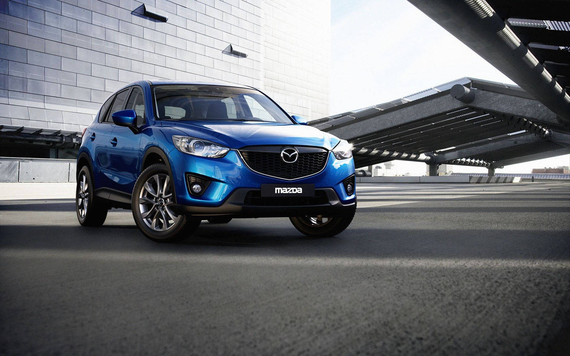 Mazda 桌布 壁紙 — 一輛鮮藍色的Mazda CX-5 SUV停放在現代鋼橋下，背景是一座時尚的灰色建築。