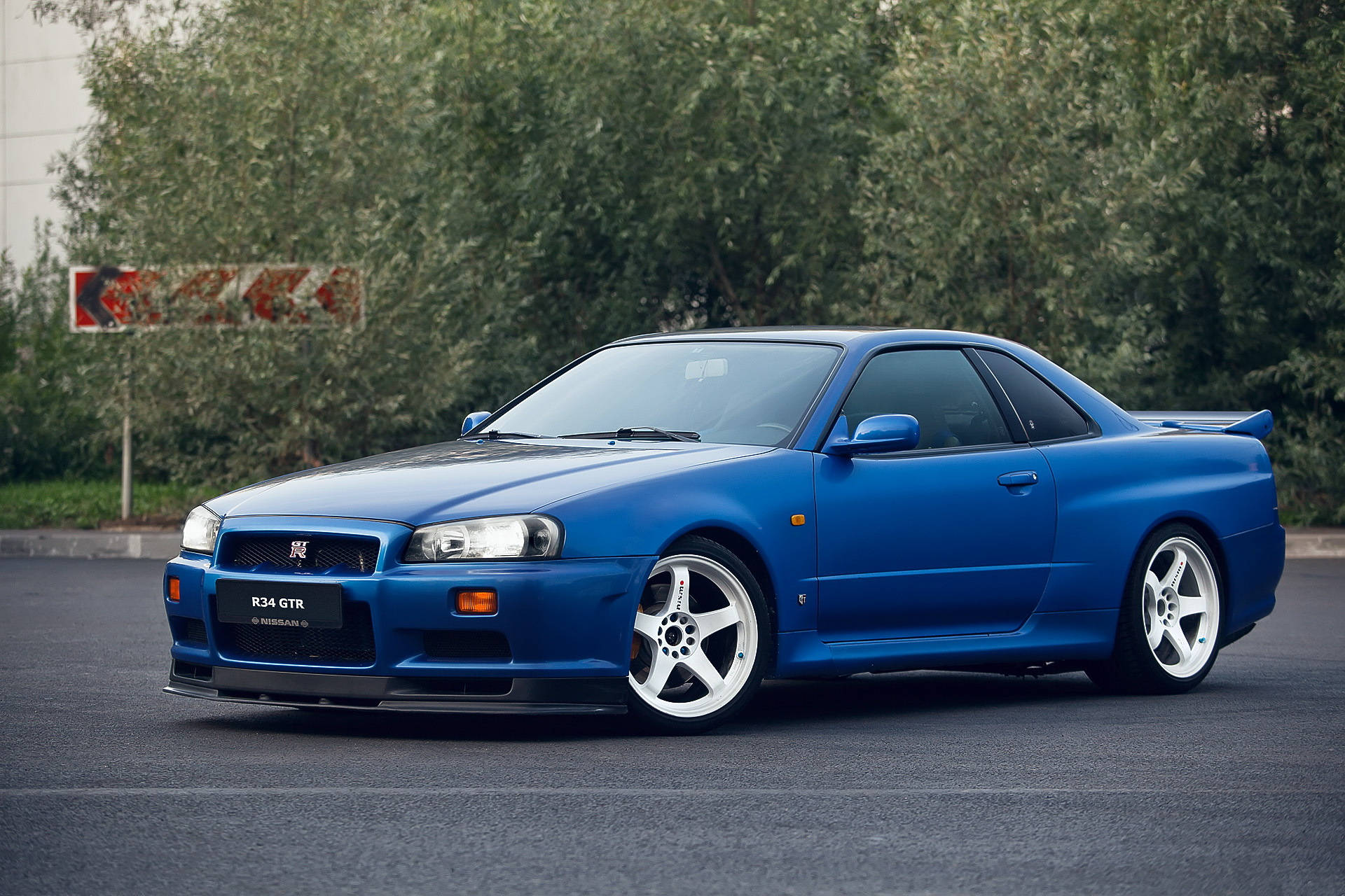 藍色日產R34 GTR跑車停在瀝青路上，靠近樹木。