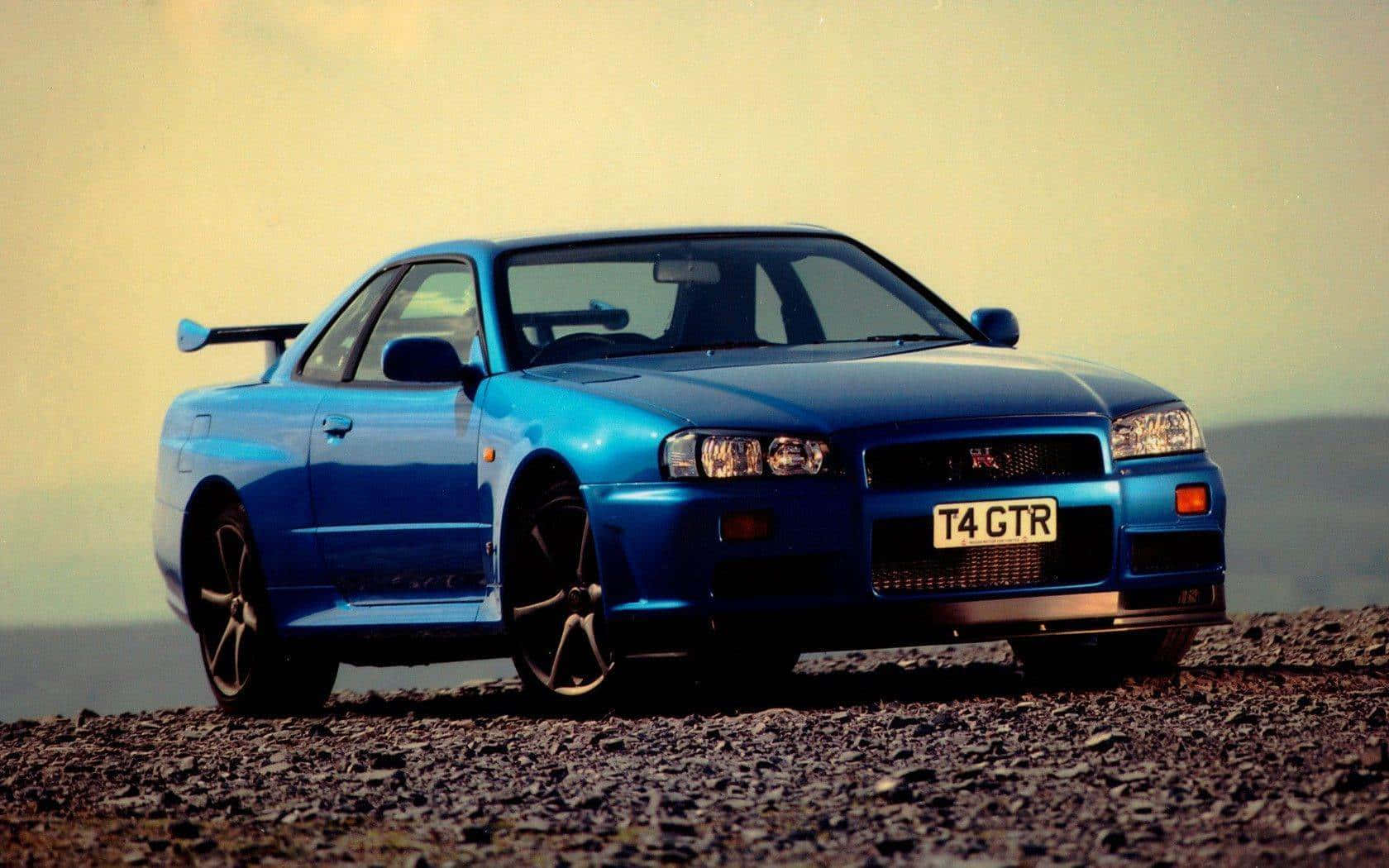 桌布 壁紙 — 一輛鮮藍色的日產Skyline R34 GTR停泊在碎石山坡上，天空朦朧。
