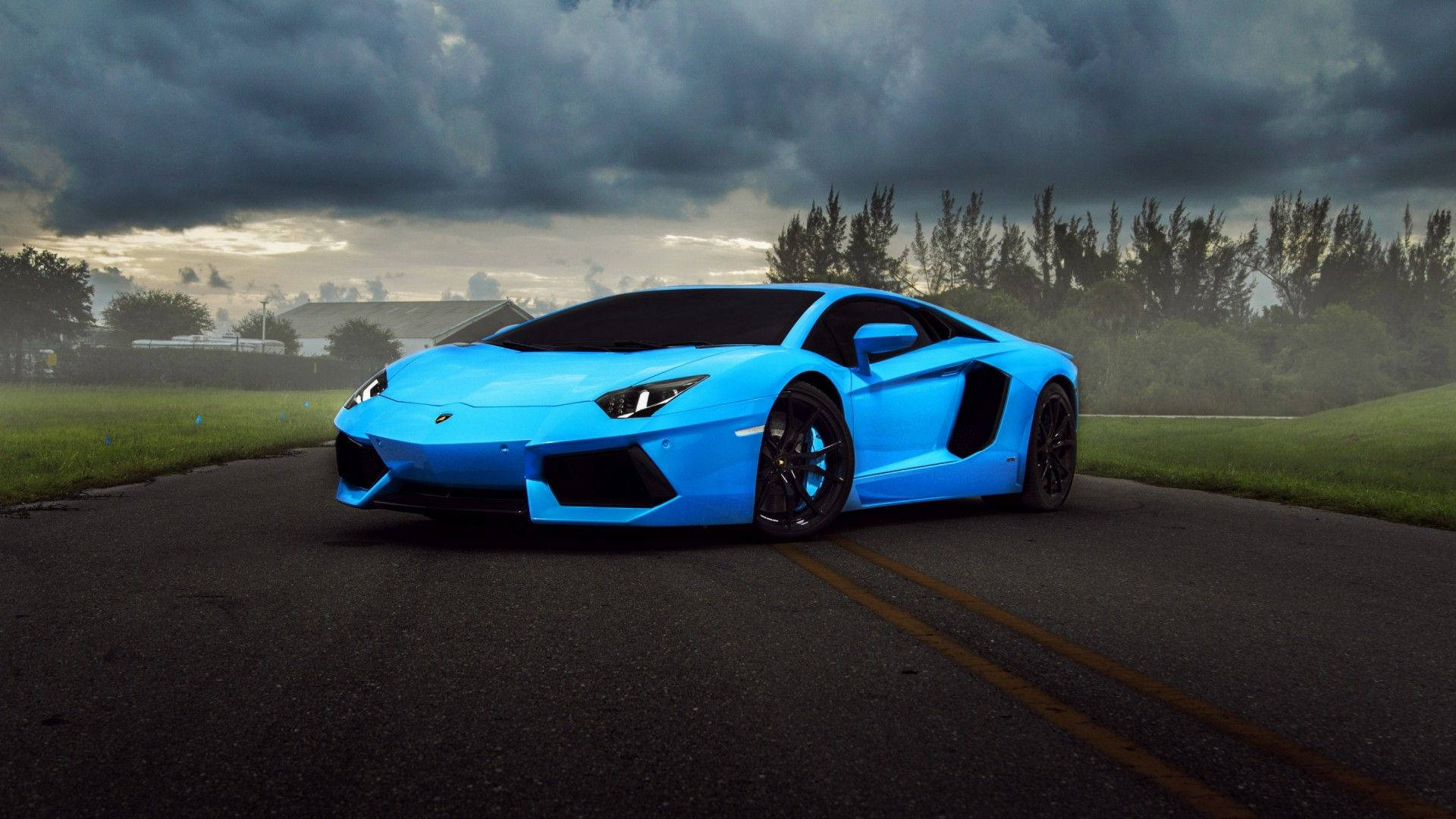 汽車 桌布 壁紙 — 一輛鮮藍色的藍寶堅尼Aventador停在濕滑的道路上，背景是戲劇性的暴風雲、綠草和樹木。