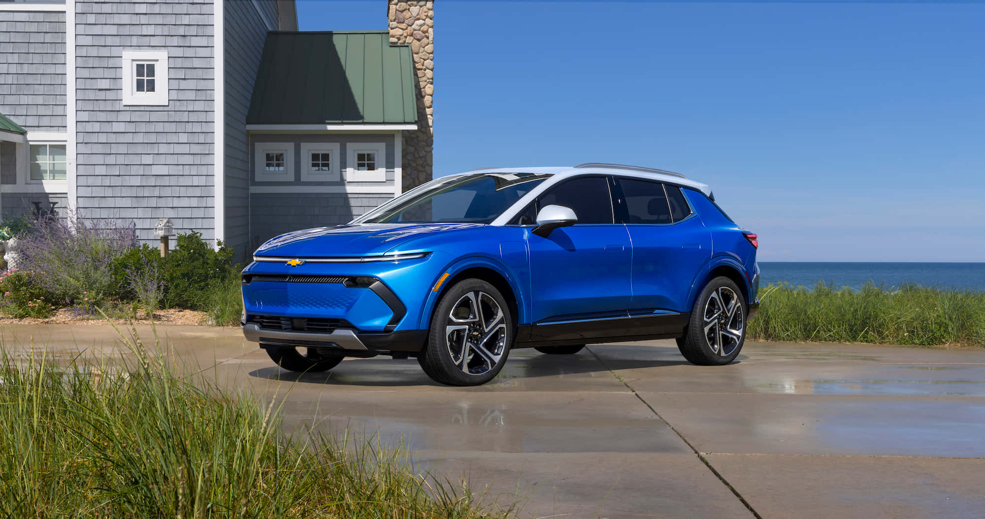 Chevrolet 桌布 壁紙 — 一輛鮮藍色的雪佛蘭SUV停放在濕漉漉的車道上，旁邊是一間享有海景的海岸房屋，天空清澈湛藍。