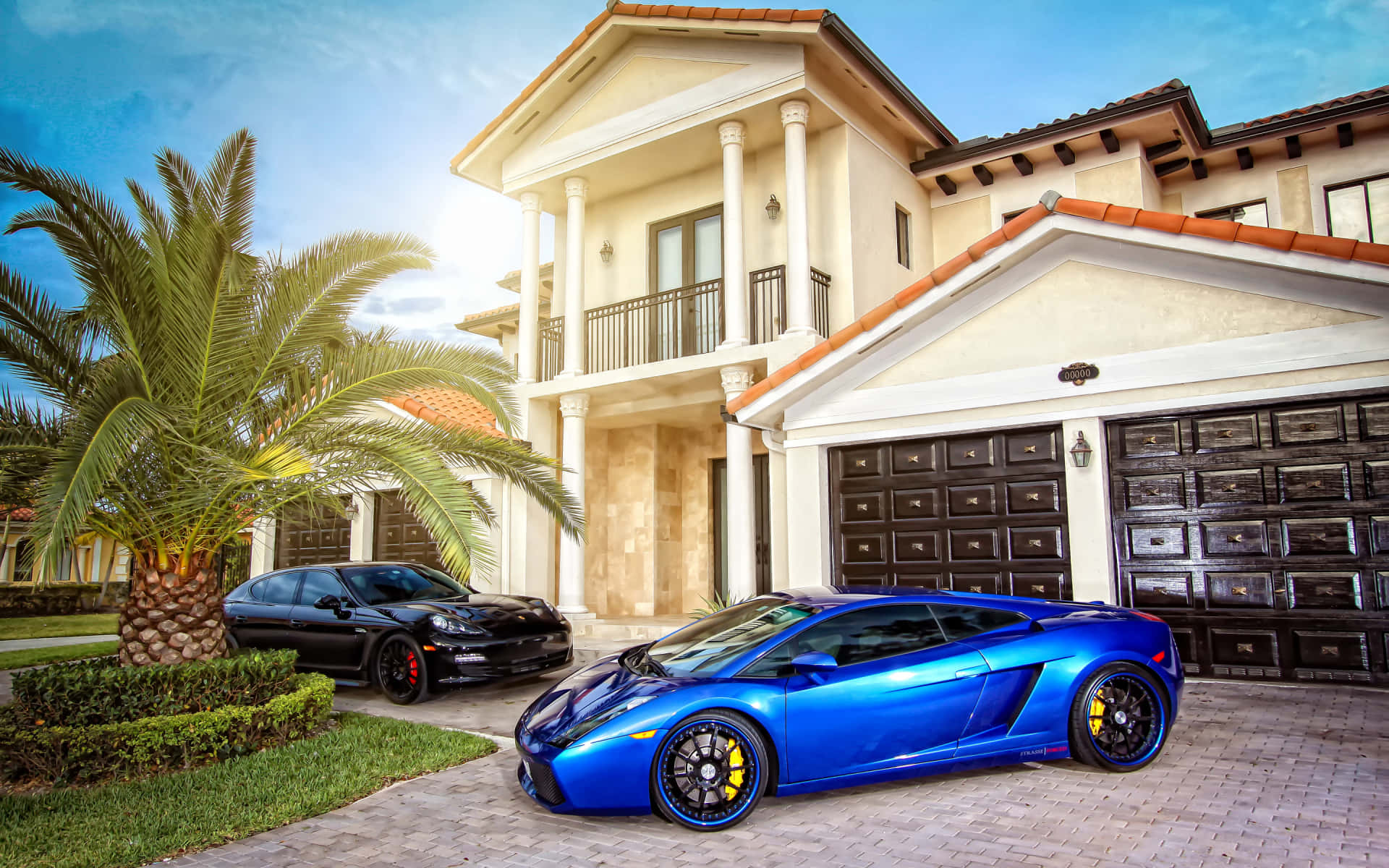 Home 桌布 壁紙 — 一輛鮮藍色藍寶堅尼Gallardo和黑色保時捷Cayman停放在磚砌車道上，前方是豪華地中海風格豪宅，種有棕櫚樹。