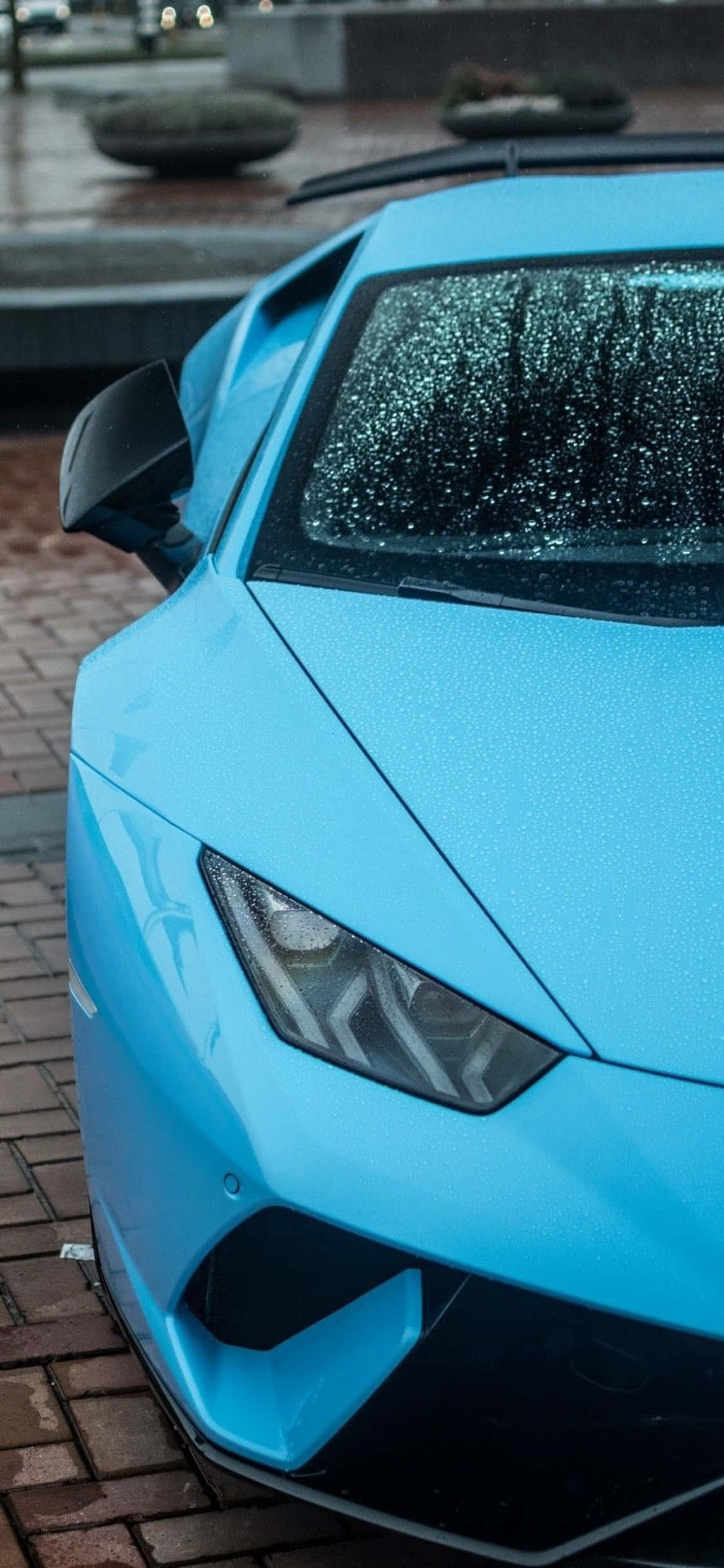 iPhone X Lamborghini 桌布 壁紙 — 一輛鮮藍色跑車停在濕磚路上，擋風玻璃上有雨滴。