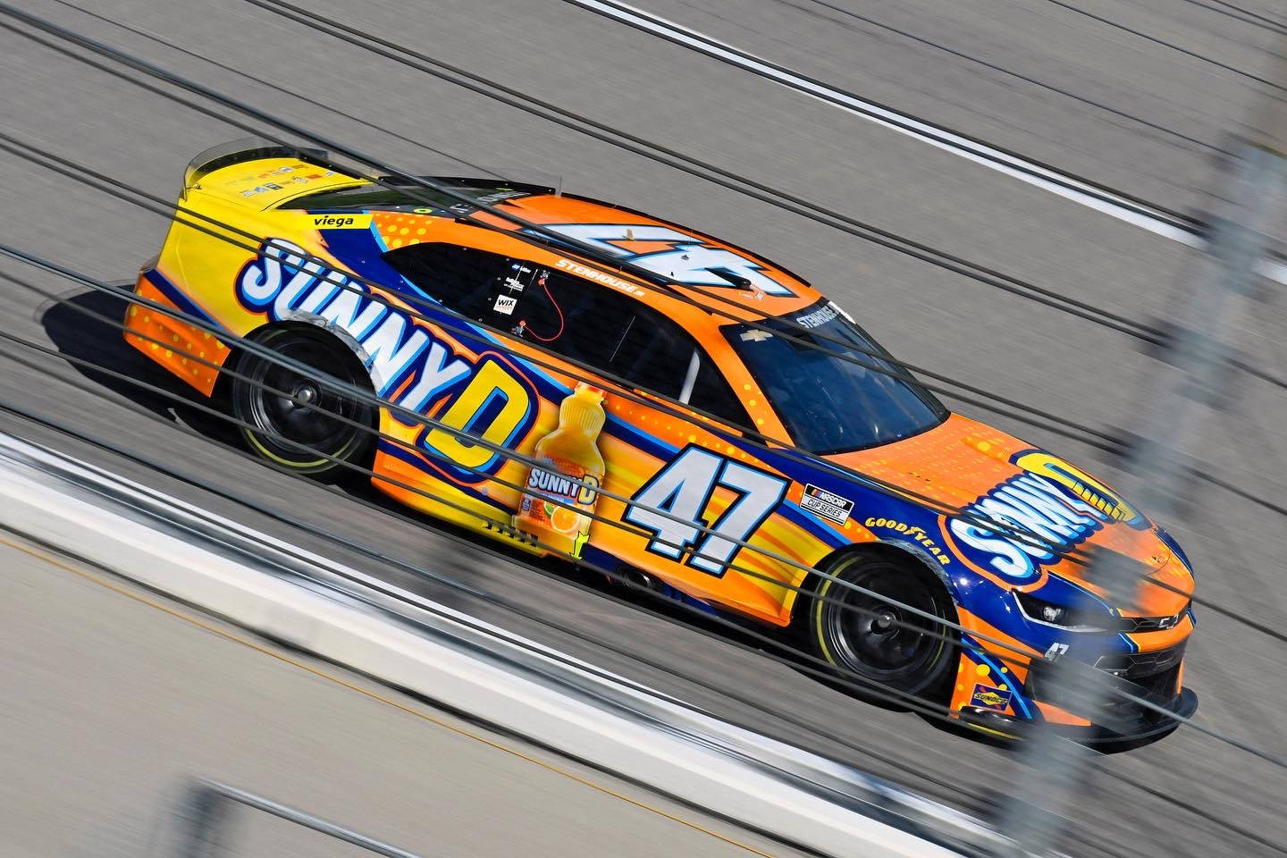 Racing 桌布 壁紙 — 一輛鮮豔的橙色、黃色和藍色Sunny D品牌賽車在賽道上疾馳，動態模糊強調其速度。