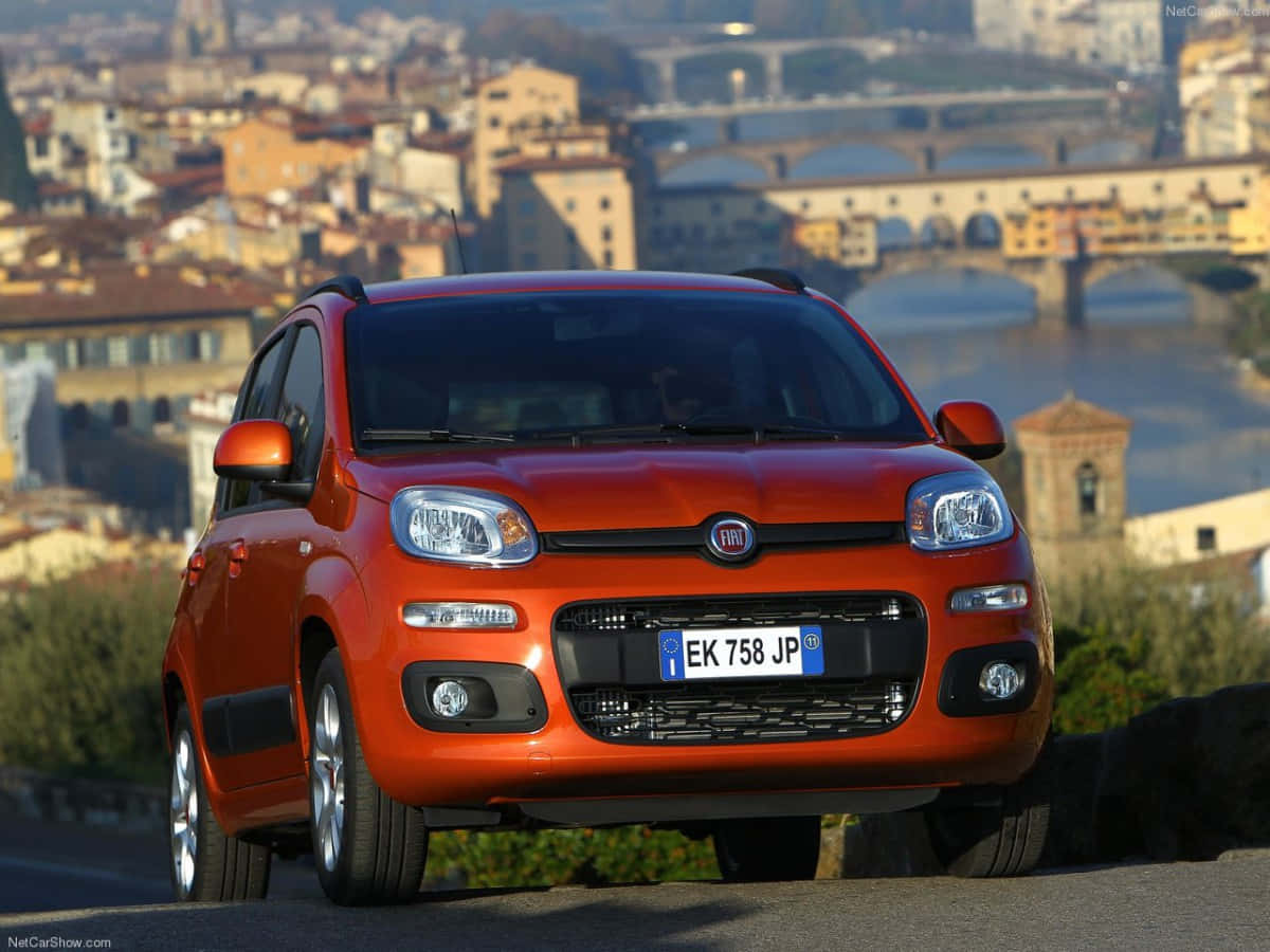 Fiat Panda 桌布 壁紙 — 一輛鮮豔的橙色Fiat Panda停泊在山坡上，俯瞰佛羅倫斯，背景是阿諾河和歷史悠久的橋樑。