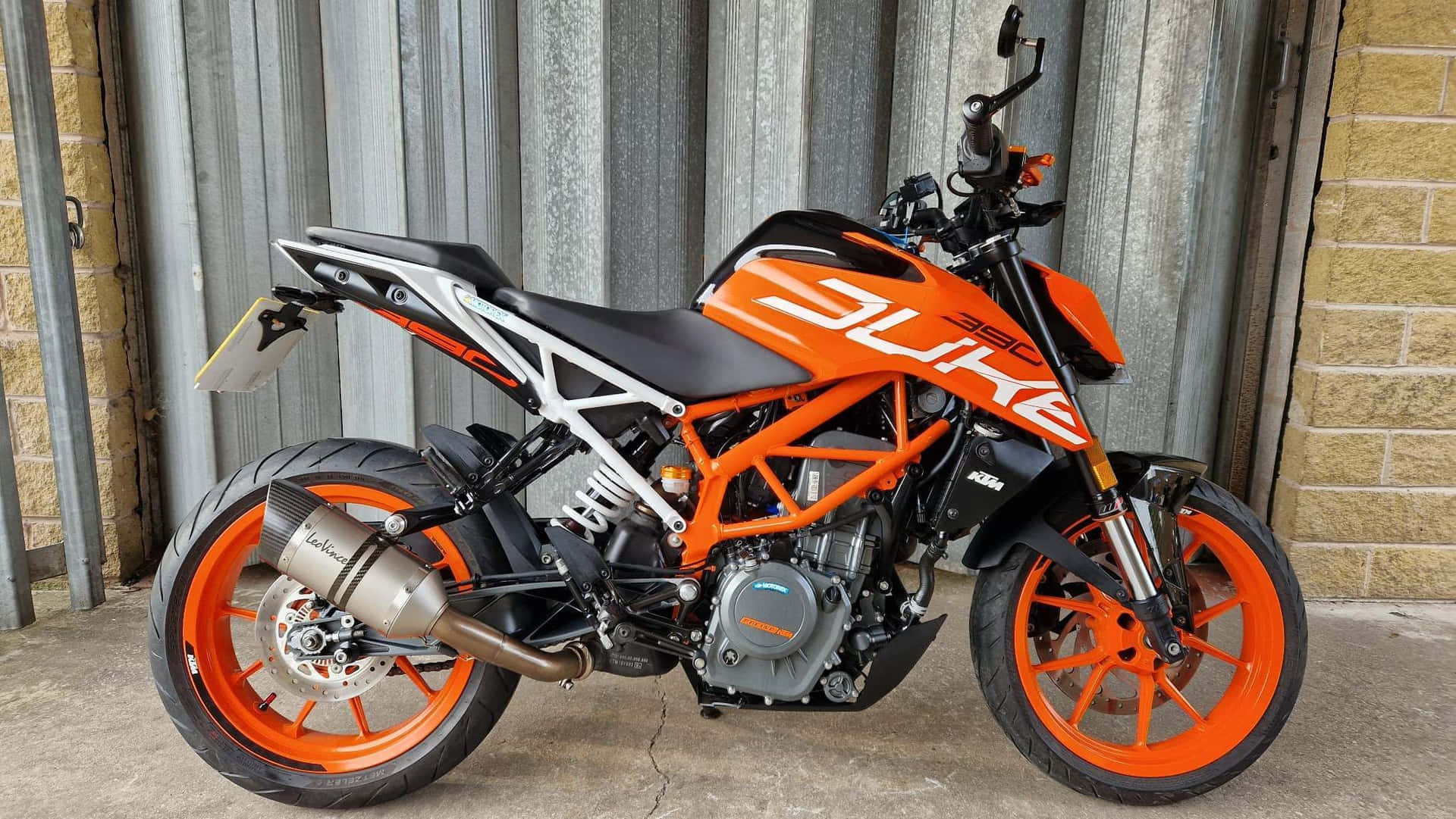  壁紙 — 一輛鮮豔的橙色KTM Duke機車停靠在波紋金屬和磚牆旁。