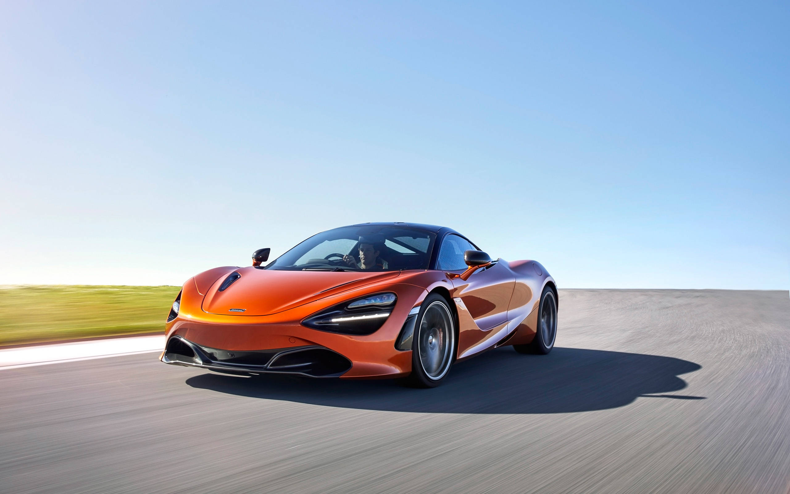 mclaren 720s 4K 桌布 壁紙 — 一輛鮮豔的橙色McLaren 720S在晴朗藍天下沿著陽光明媚的沙漠公路飛馳。