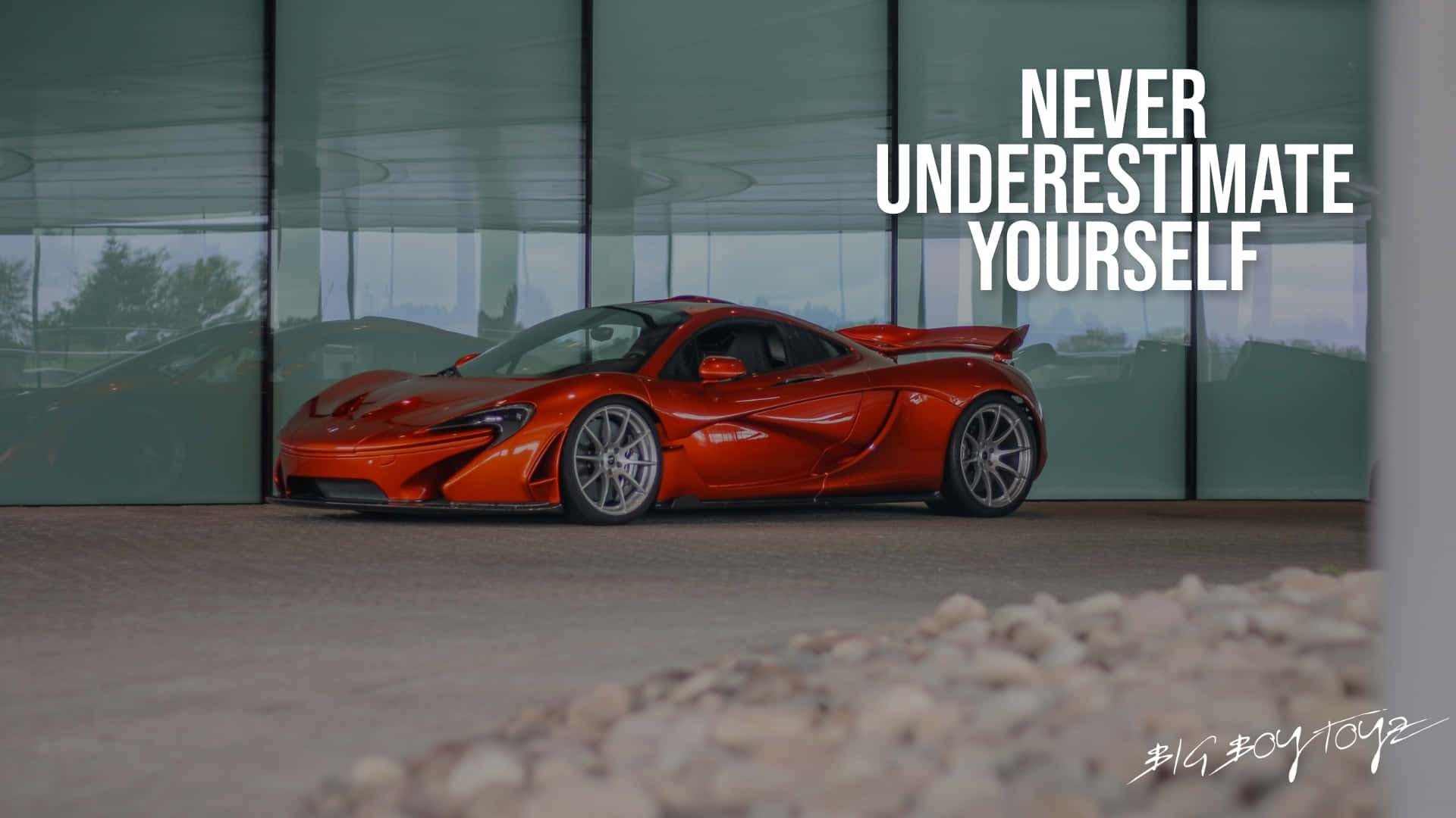 高清汽車 桌布 壁紙 — 一輛鮮豔的橙色McLaren P1超級跑車停在室內玻璃牆前，上面醒目地顯示著勵志文字「永遠不要低估自己」。
