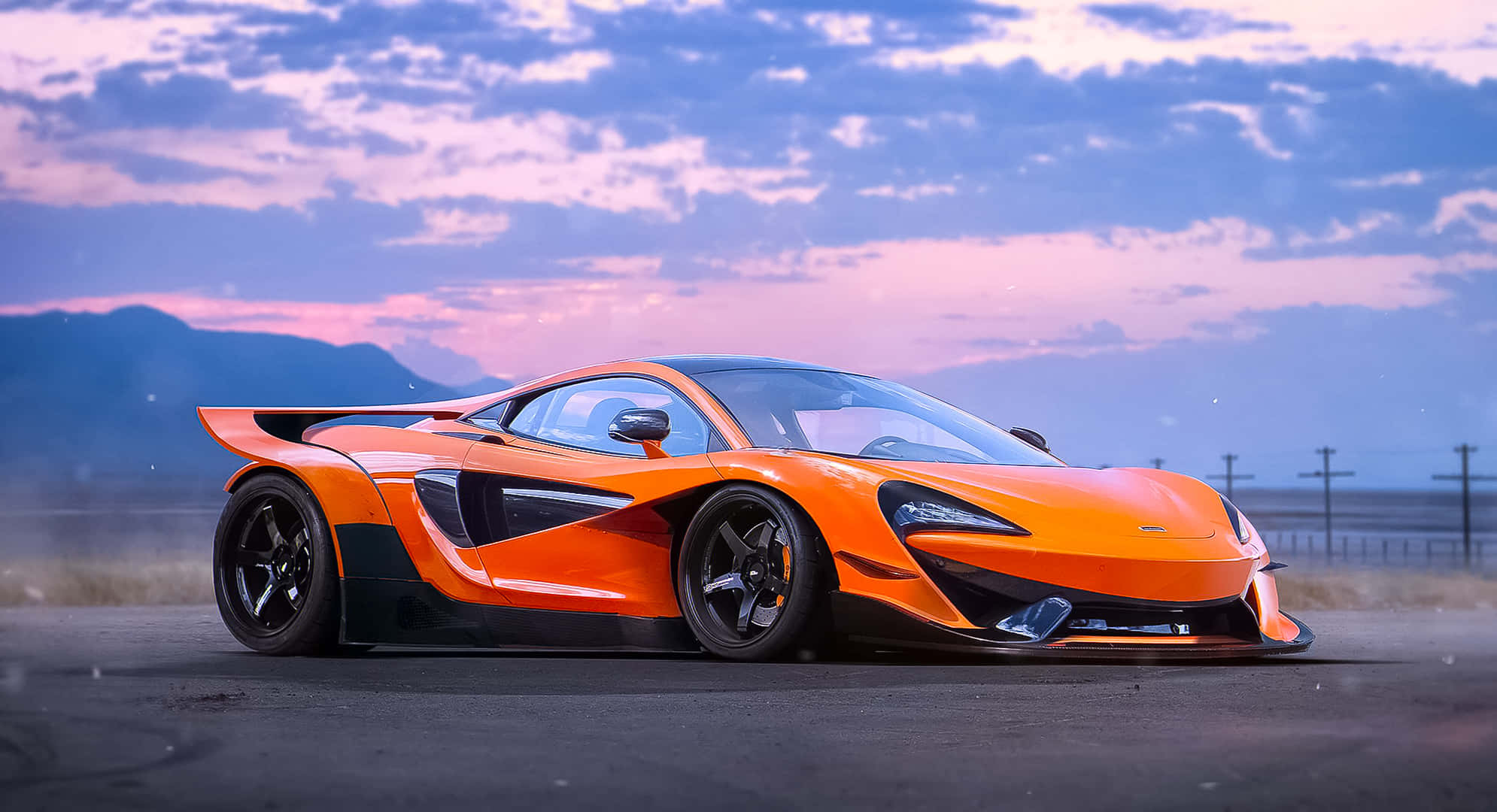麥拉倫 桌布 壁紙 — 一輛鮮豔的橙色McLaren P1超級跑車在暮色天空下閃耀，天空中有紫色和粉紅色的雲彩，遠處是山脈。