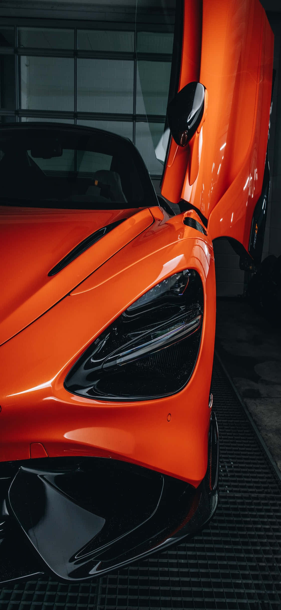 麥拉倫 桌布 壁紙 — 一輛鮮豔的橙色McLaren跑車，車門向上打開，停放在一個具有反光表面的現代車庫內。
