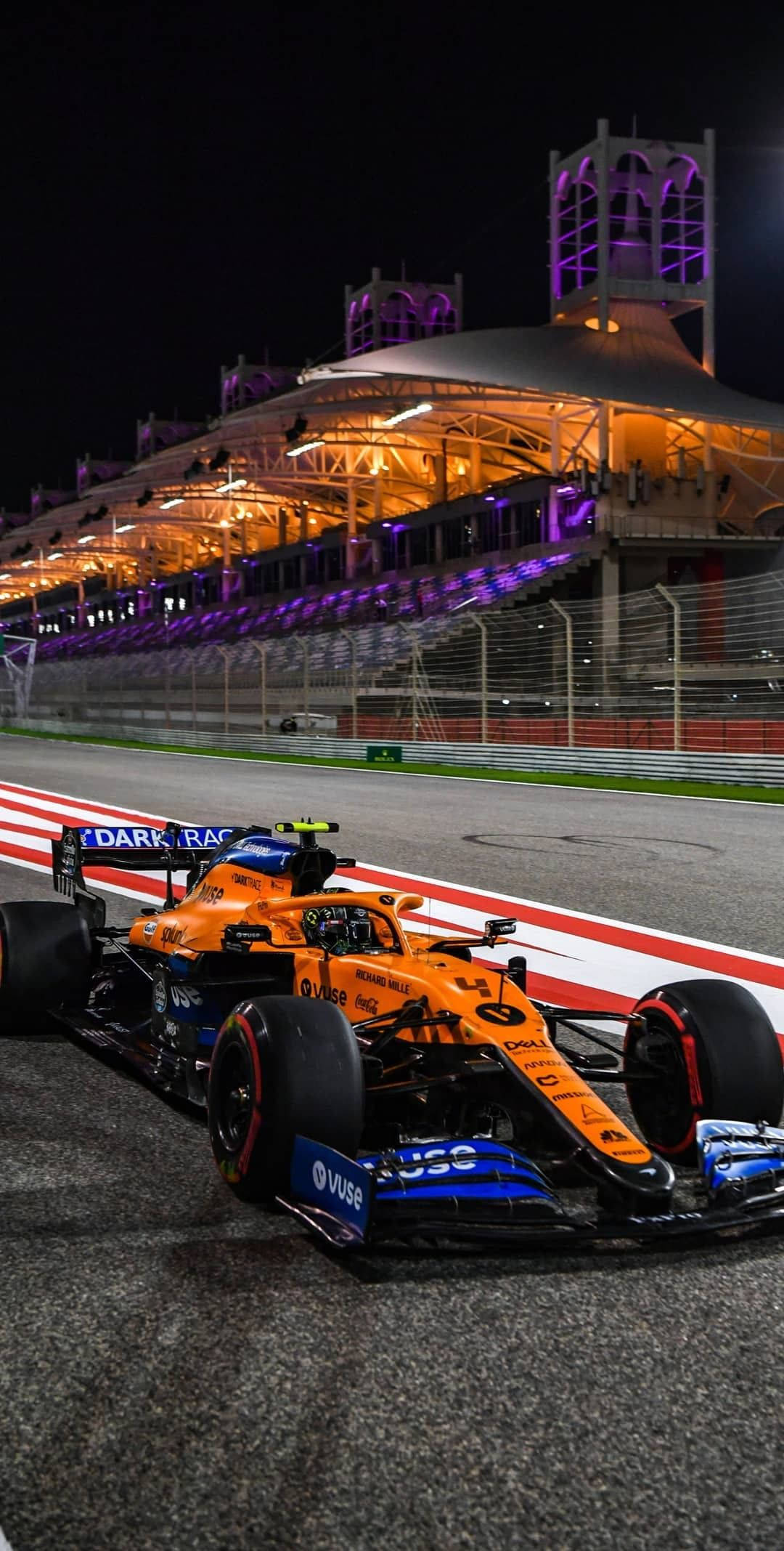 Racing 桌布 壁紙 — 一輛鮮豔的橙色和藍色一級方程式賽車在夜間停放在賽道上，下方是紫色燈光照亮的看台。