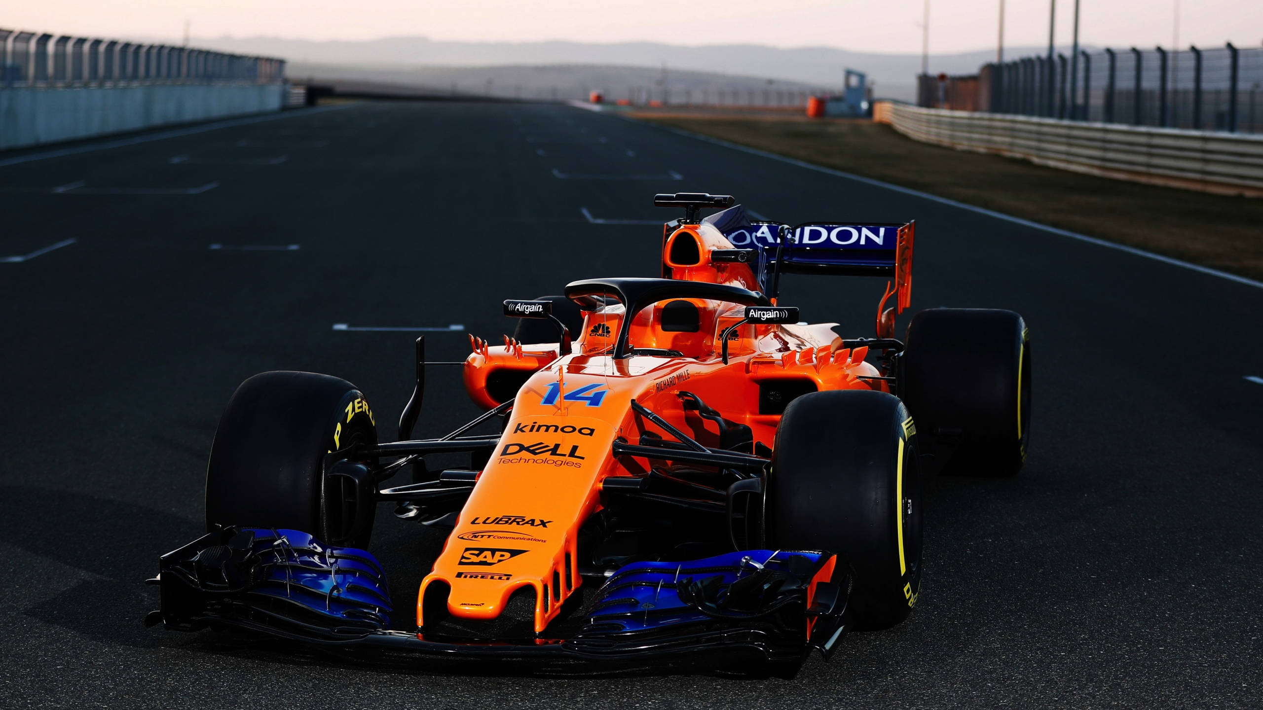 Formula One 桌布 壁紙 — 一輛鮮豔的橙色和藍色一級方程式賽車（14號）在黃昏時分沿著賽道疾馳。