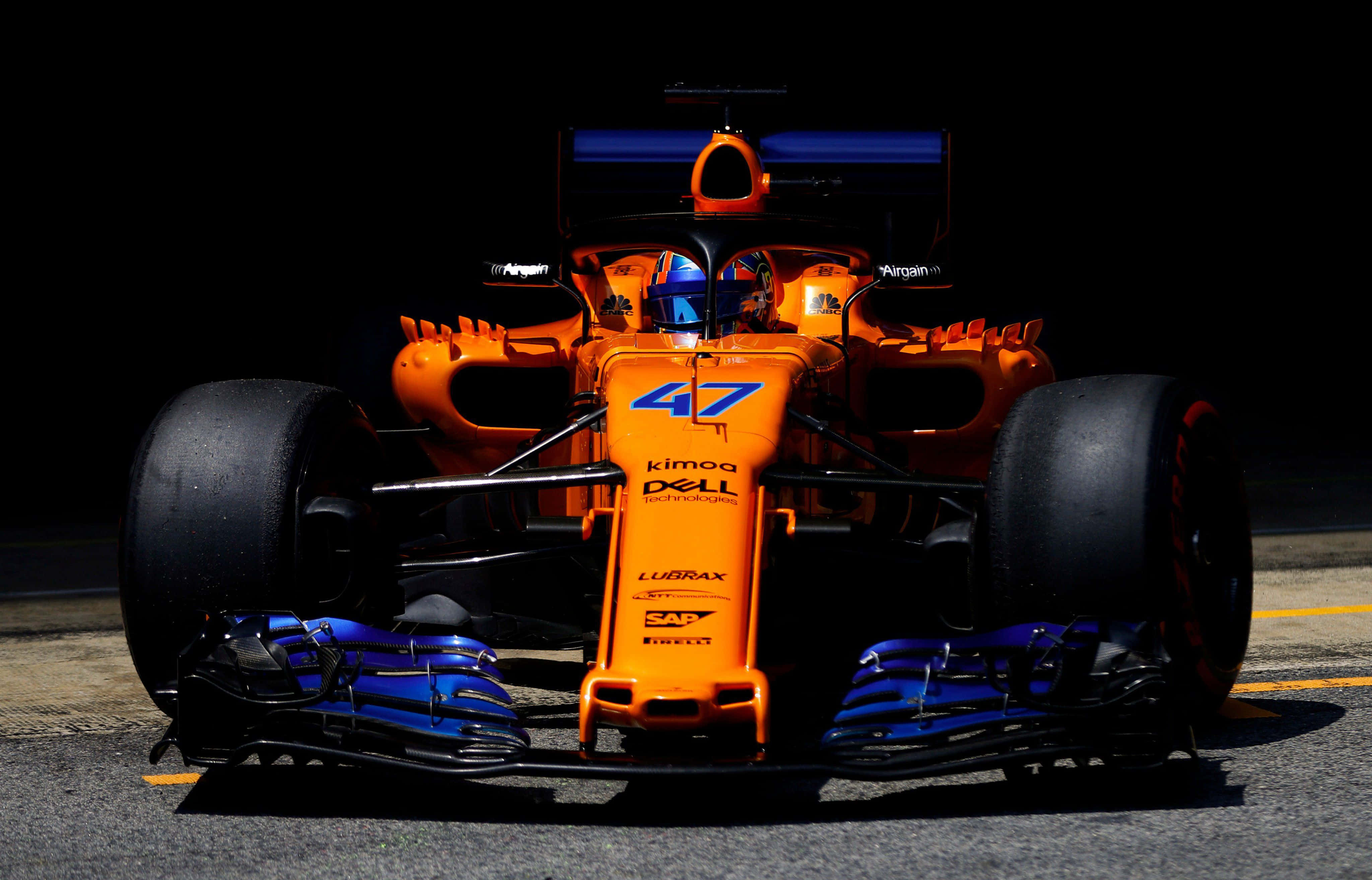 lando norris 桌布 壁紙 — 一輛鮮豔的橙色和藍色一級方程式賽車（編號47）在賽道上以黑暗背景為襯托，戲劇性地被照亮。
